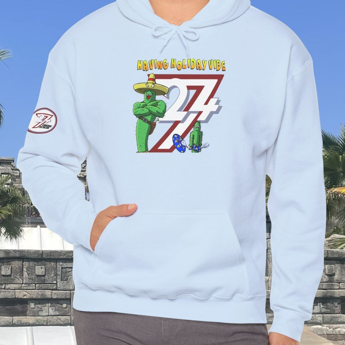 Adult wearing light blue cactus hoodie with cartoon graphic and holiday vibe text outdoors