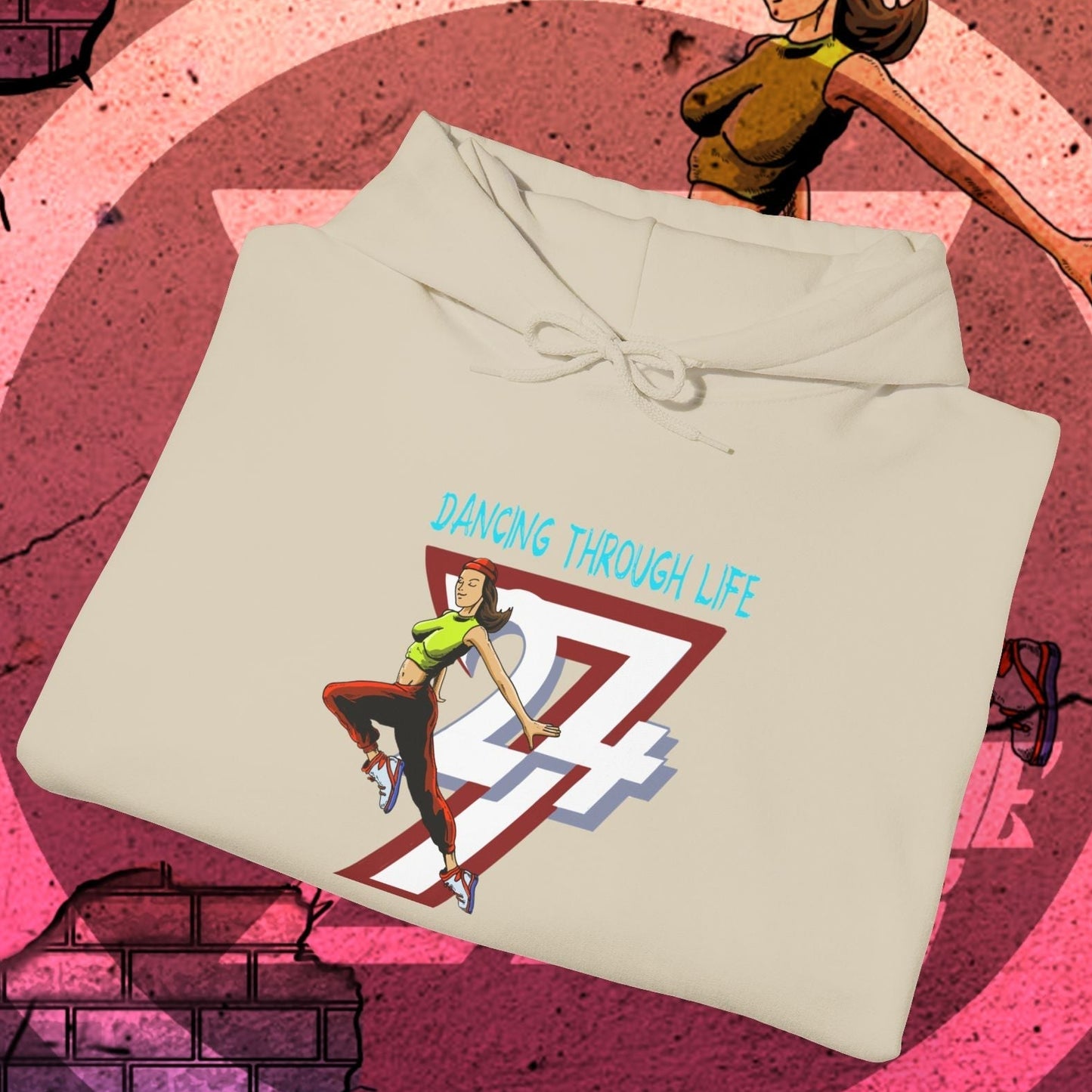 Folded beige street dance hoodie for women with dancing illustration and "Dancing Through Life" text on an urban graffiti background