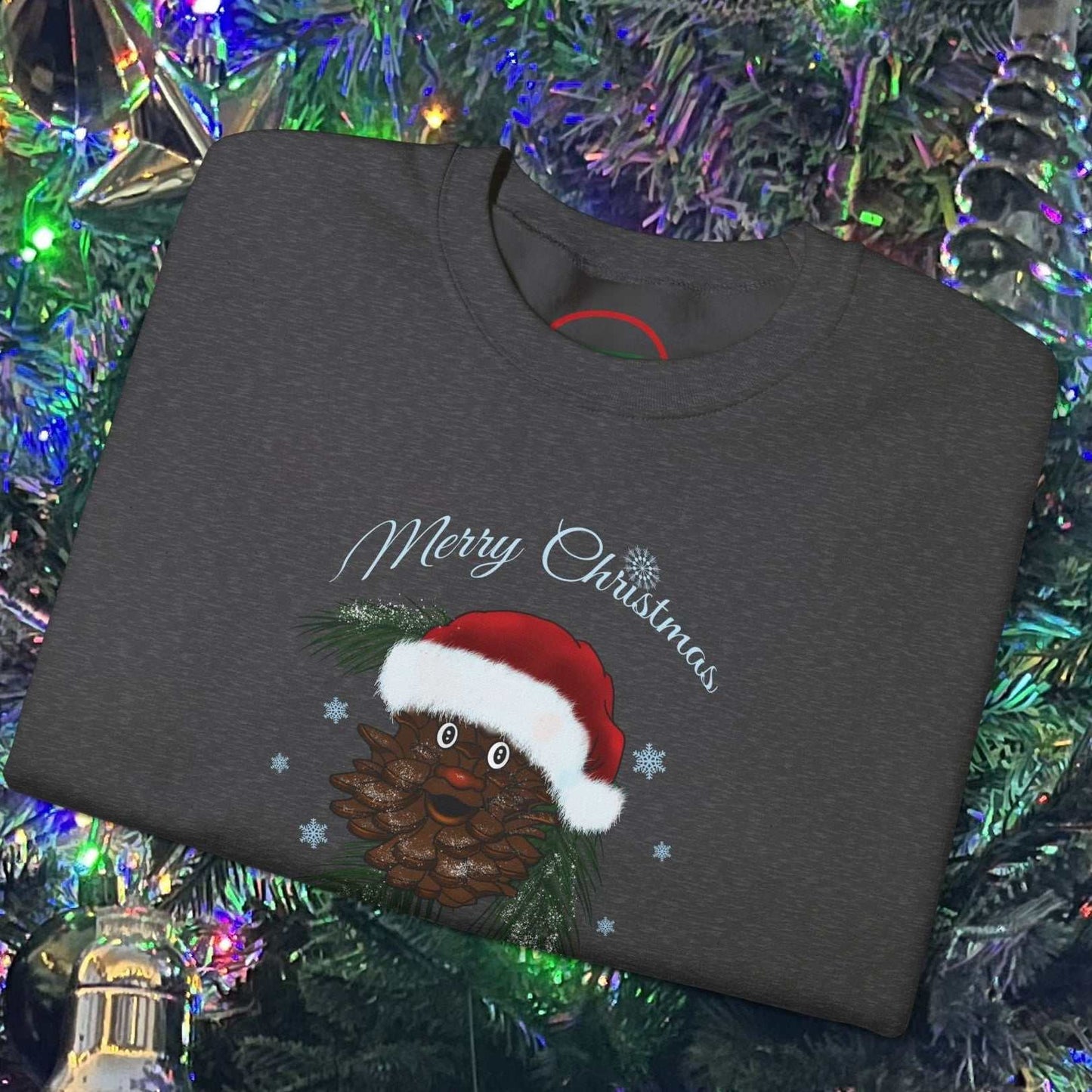 Folded dark gray Santa Pinecone Christmas Sweatshirt with hand-drawn pinecone wearing Santa hat and "Merry Christmas" text on a decorated Christmas tree background