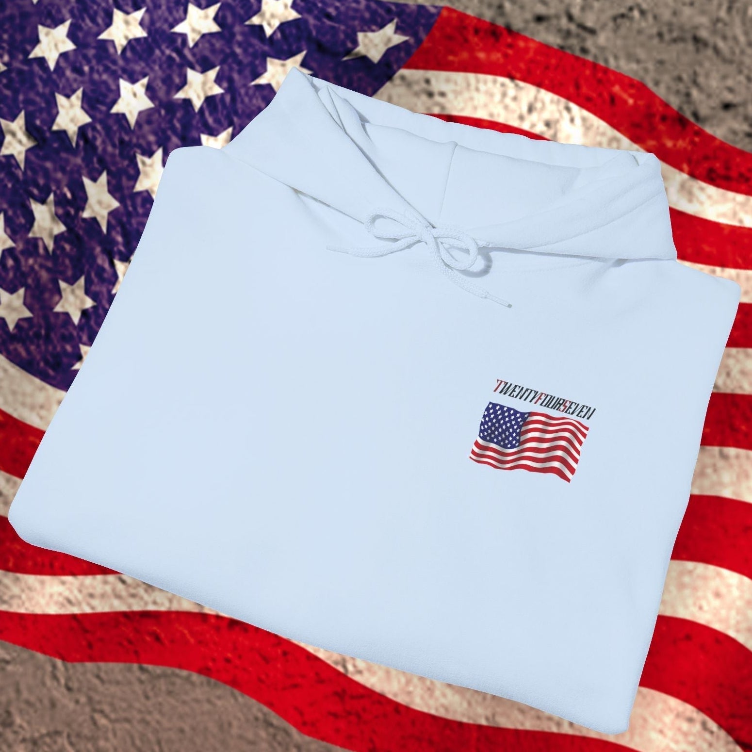Folded light blue american flag hoodie with small US flag logo on front, placed on a worn American flag background