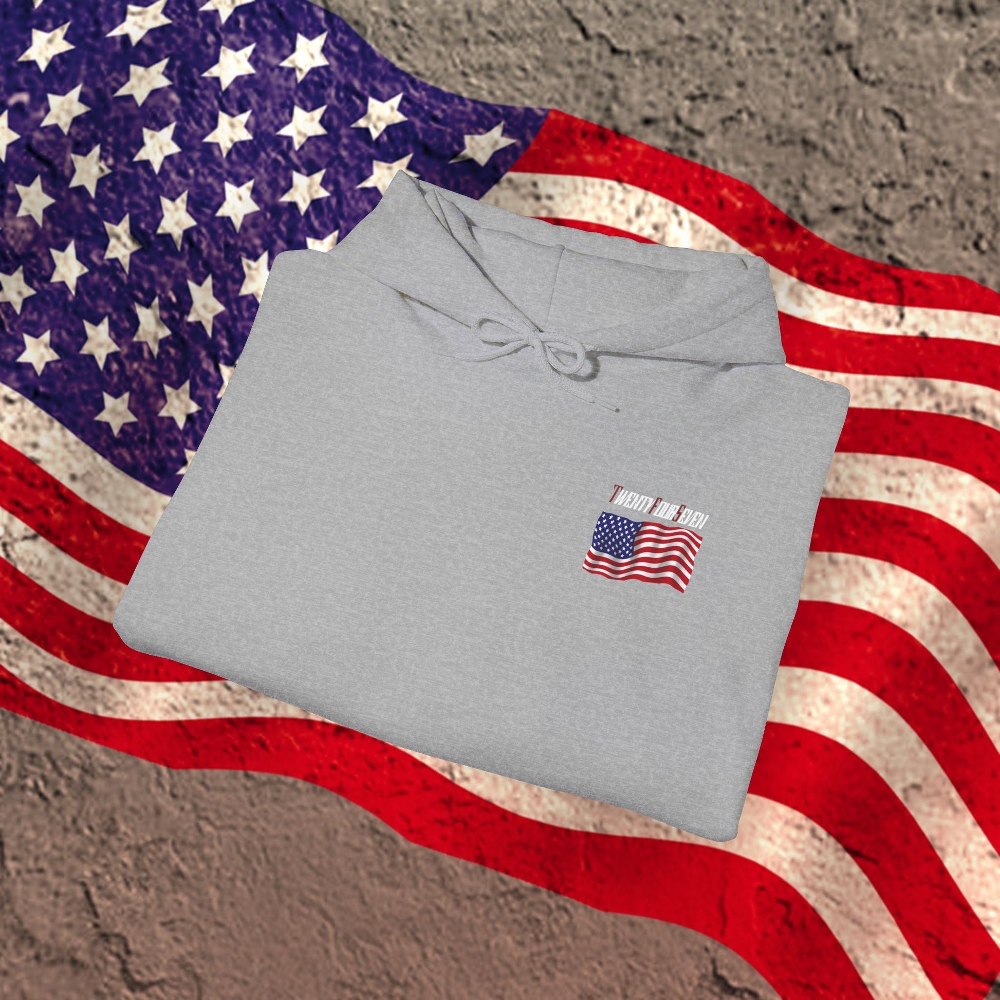 Gray US flag hoodie with small American flag design on chest, folded on large American flag background