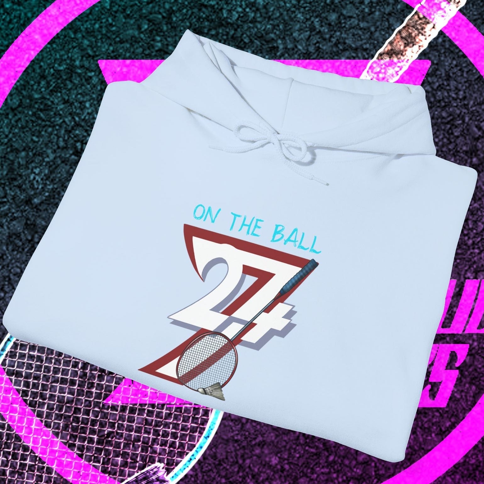 Light blue badminton hoodie with "On the Ball" graphic folded on badminton-themed background
