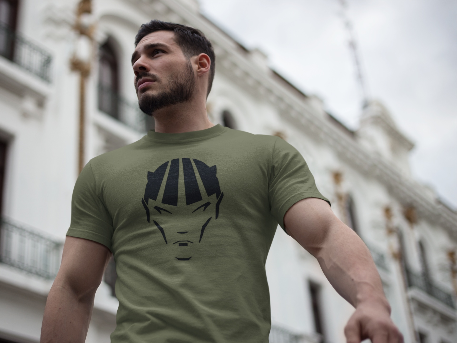 Man wearing olive green devil shirt with black comic character design outdoors