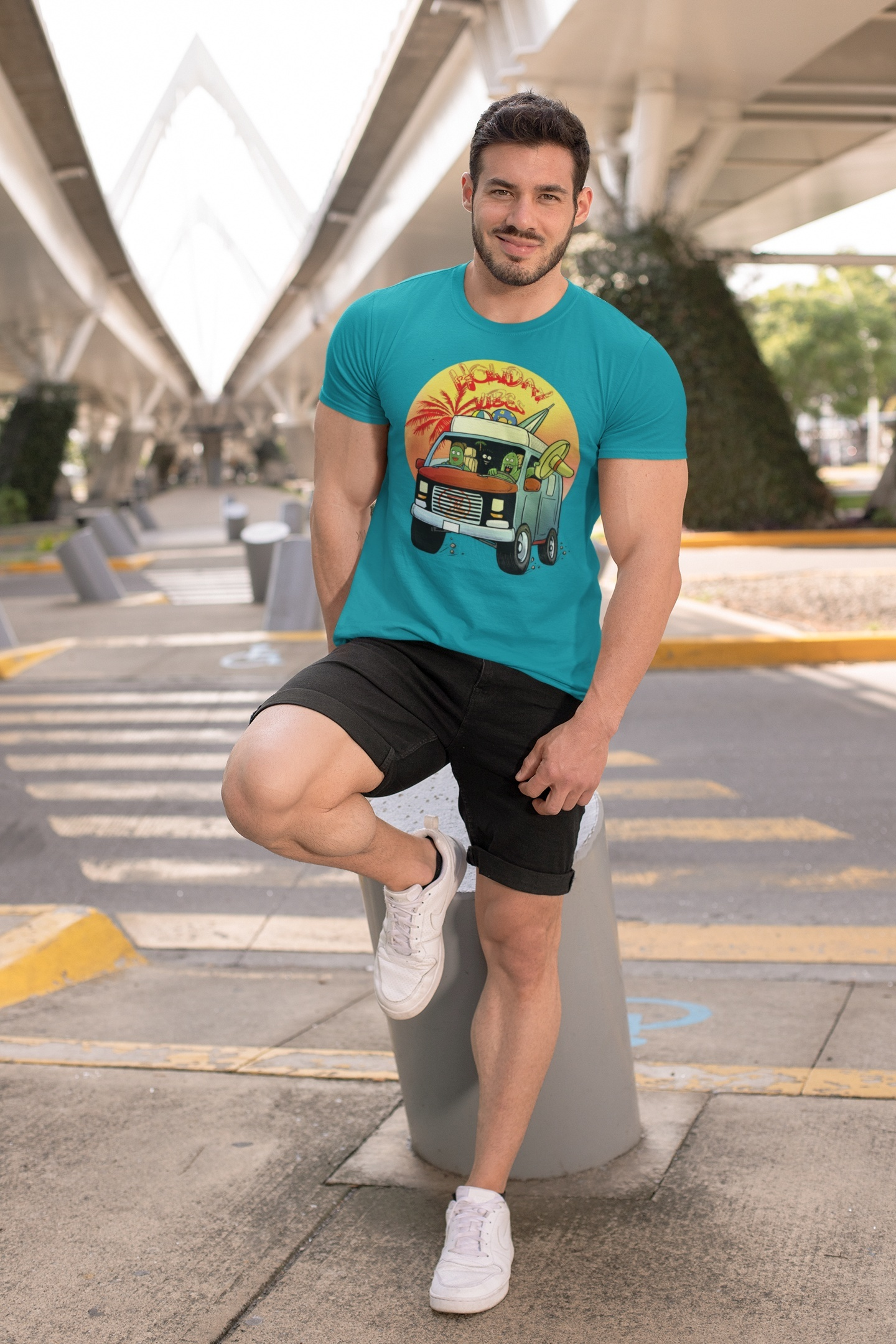 Man wearing turquoise cactus shirt with cartoon caravan design, black shorts, and white sneakers outdoors