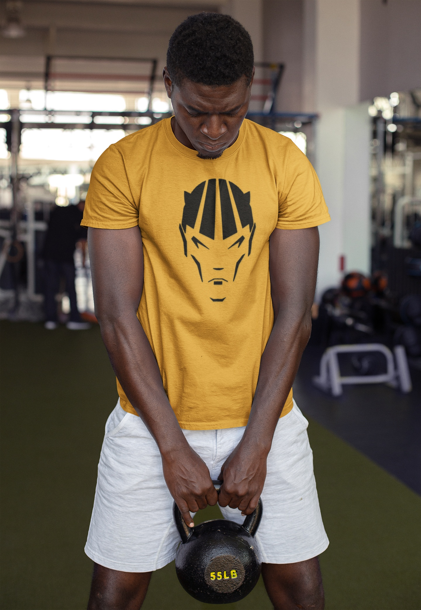 Man wearing yellow devil shirt with black comic character design lifting a 55lb kettlebell in gym