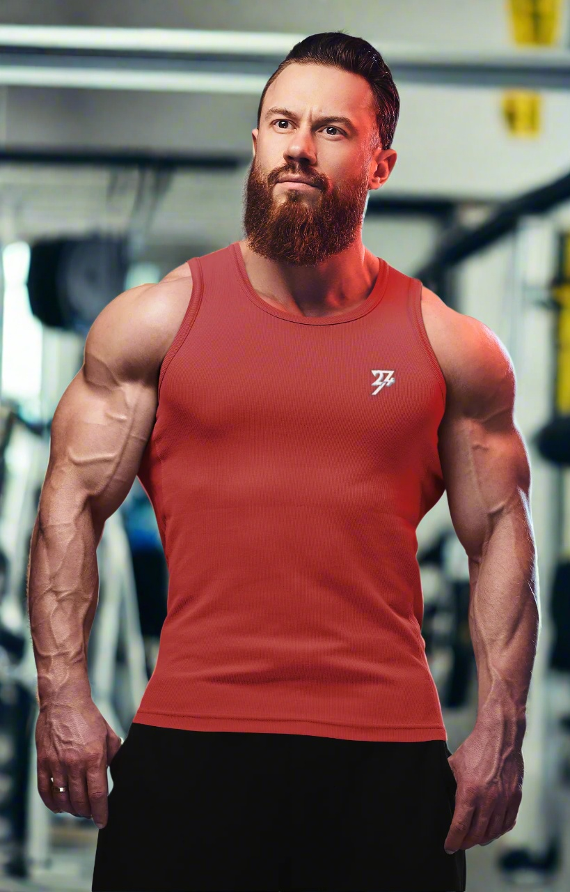 Muscular man wearing a fitted red workout tank top in gym setting, showcasing athletic and casual fitness apparel.