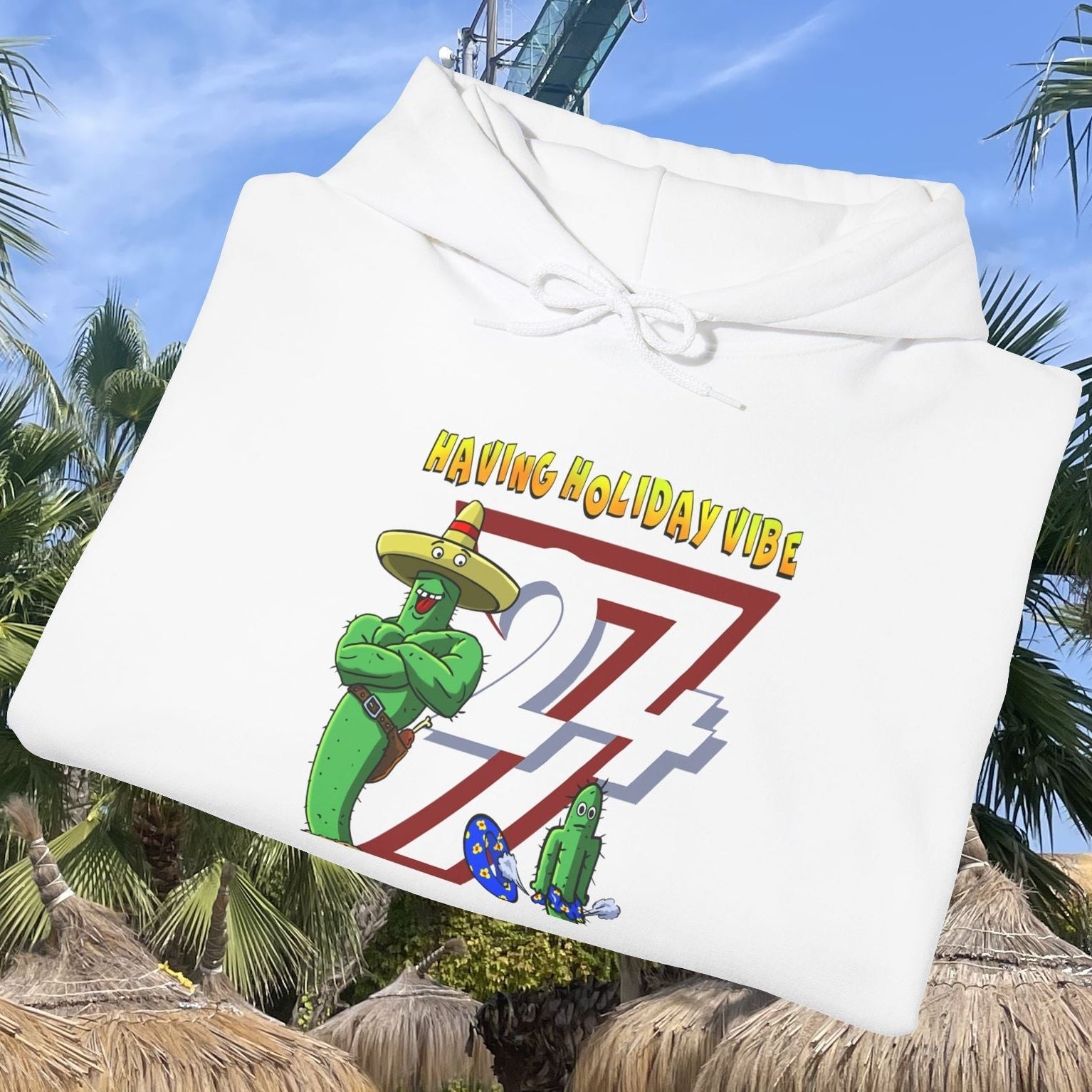 White cactus hoodie with cartoon design and holiday vibe text, folded on tropical background