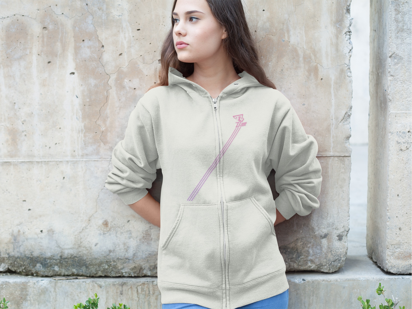 Woman wearing a gray zip hoodie with pink diagonal stripes and kangaroo pockets standing against a concrete wall, casual streetwear style women hoodie