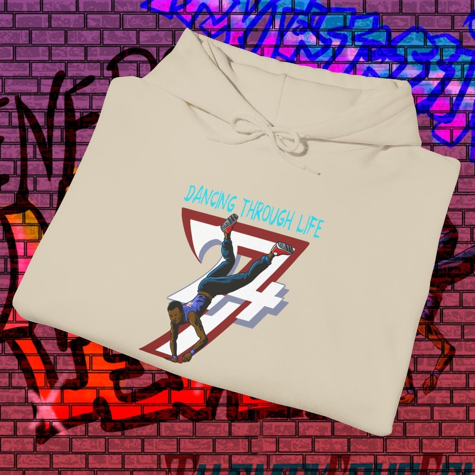 beige street dance hoodie with hand-drawn breakdancer and "Dancing Through Life" text on urban graffiti background