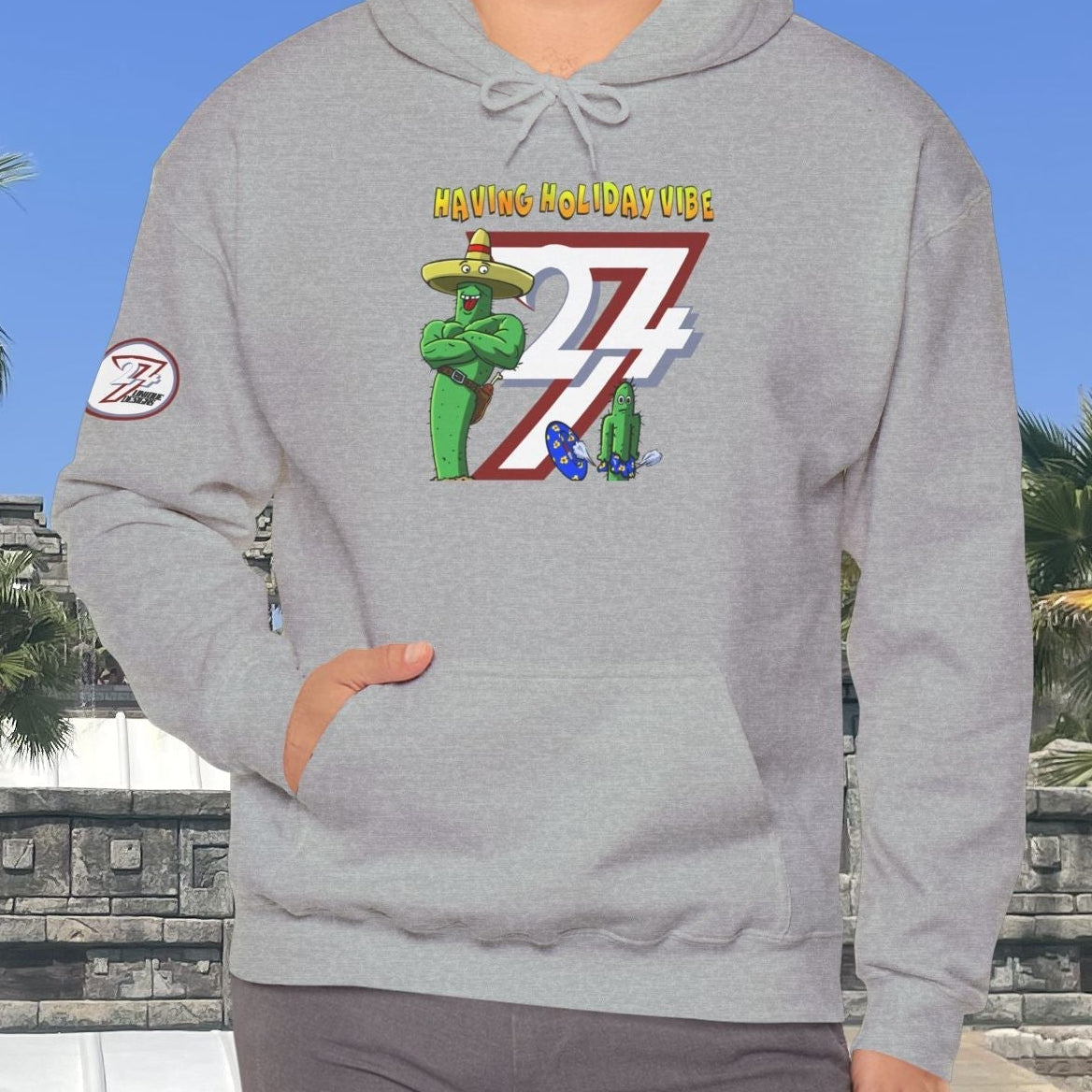 man wearing grey cactus hoodie with cartoon design and holiday vibe text