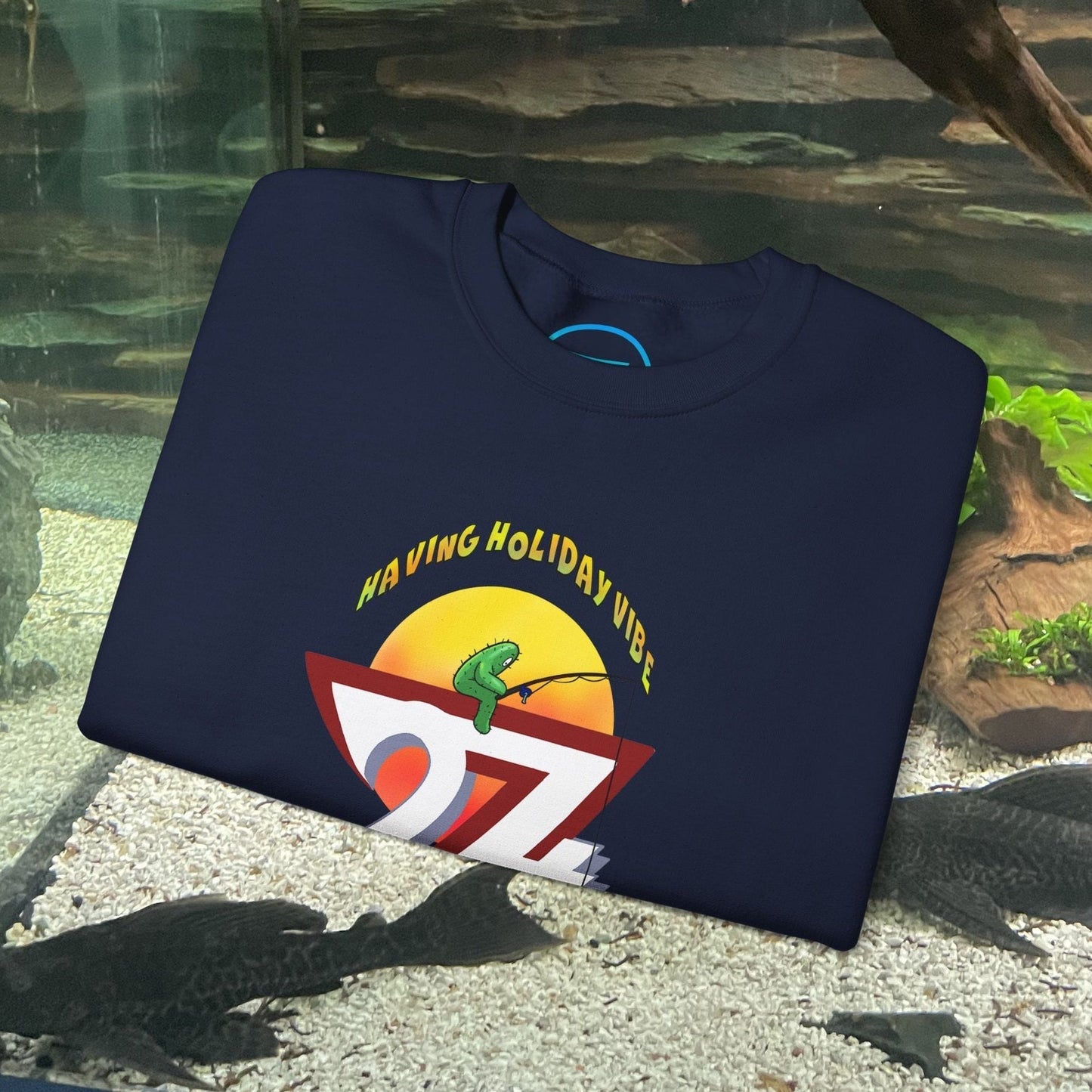 navy fishing cactus sweatshirt with colorful cartoon design and "Having Holiday Vibe" text folded on aquarium background