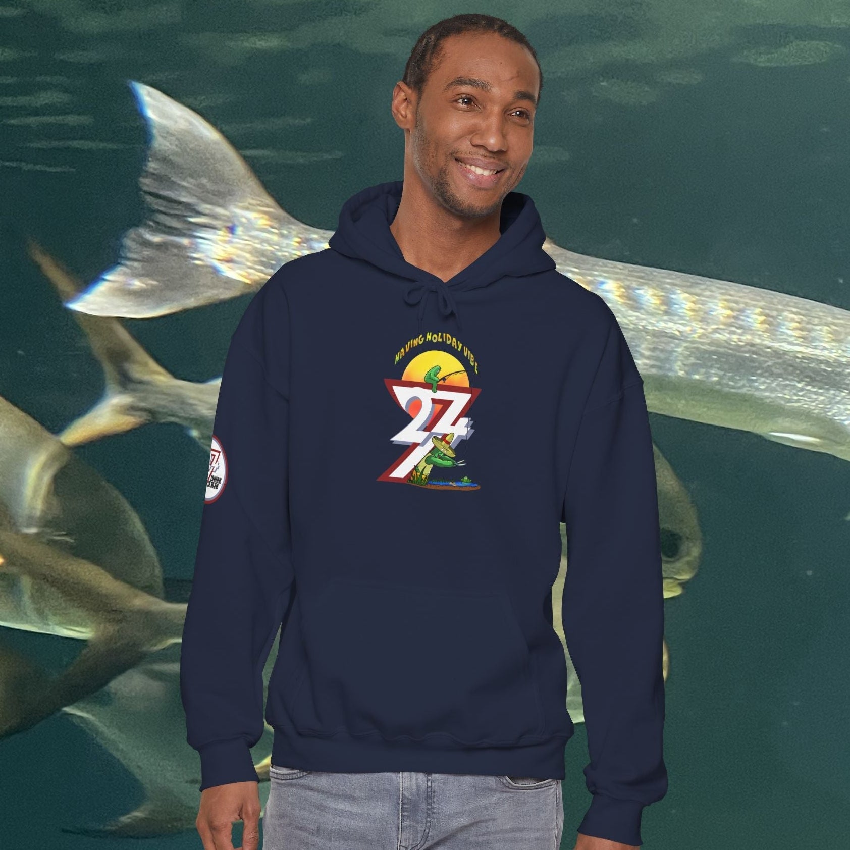 Man wearing navy funny fishing hoodie with cactus design standing in front of fish aquarium background