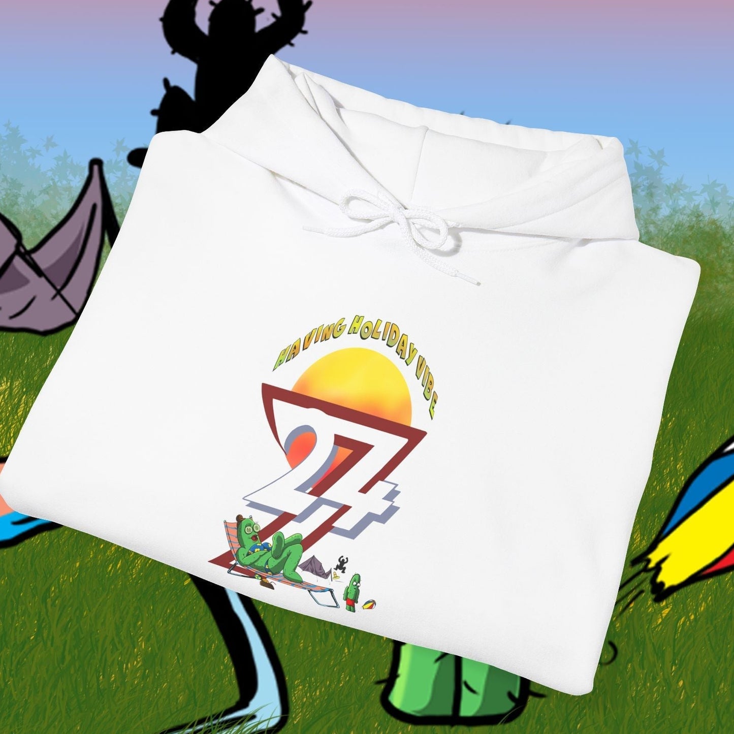 white cactus hoodie with cartoon character and camping design folded on grass background with tents and beach ball