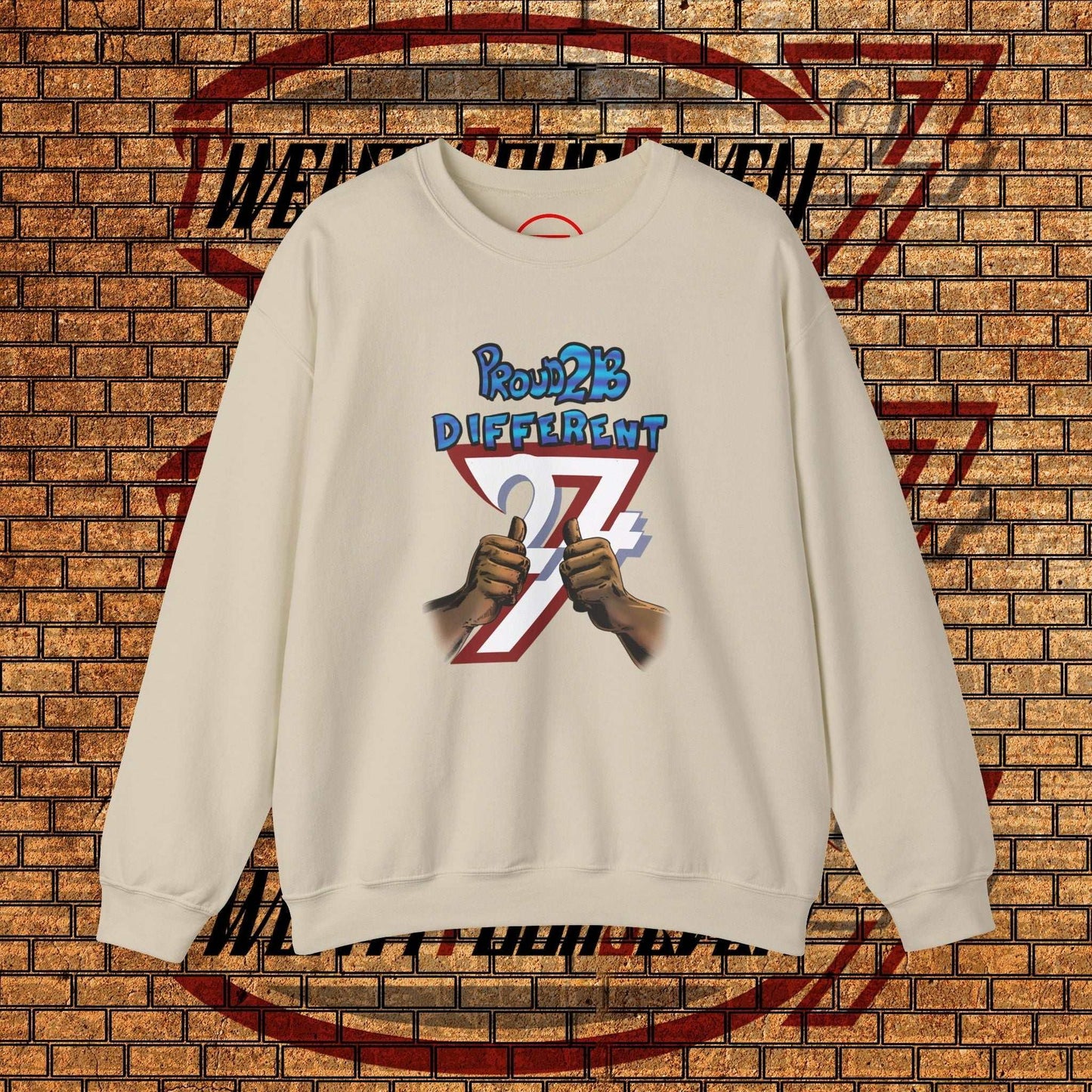 Artistic sweatshirt cream crewneck with "Proud 2 B Different" slogan and hand-drawn graphic on front against brick wall background