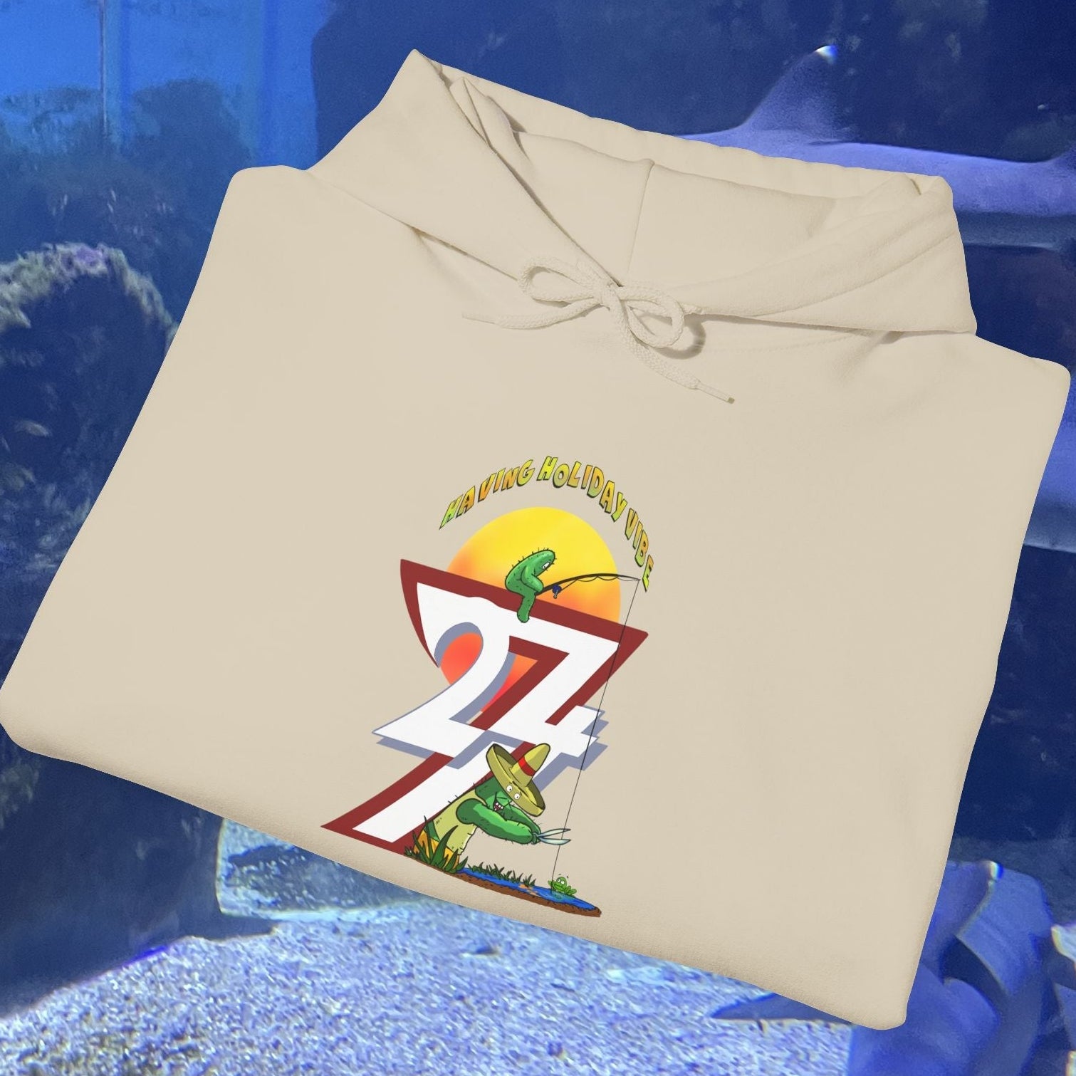 Beige funny fishing hoodie with summer holiday cactus and fishing design, folded on aquarium background