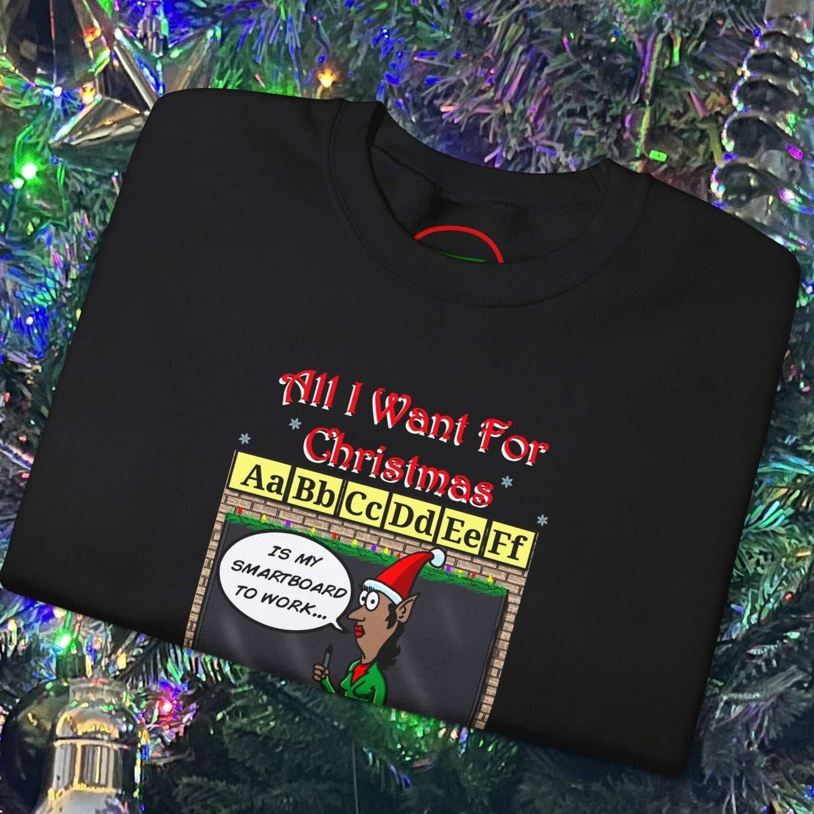 Black Christmas teacher comic sweatshirt with funny cartoon and "All I Want For Christmas" text folded on decorated Christmas tree background