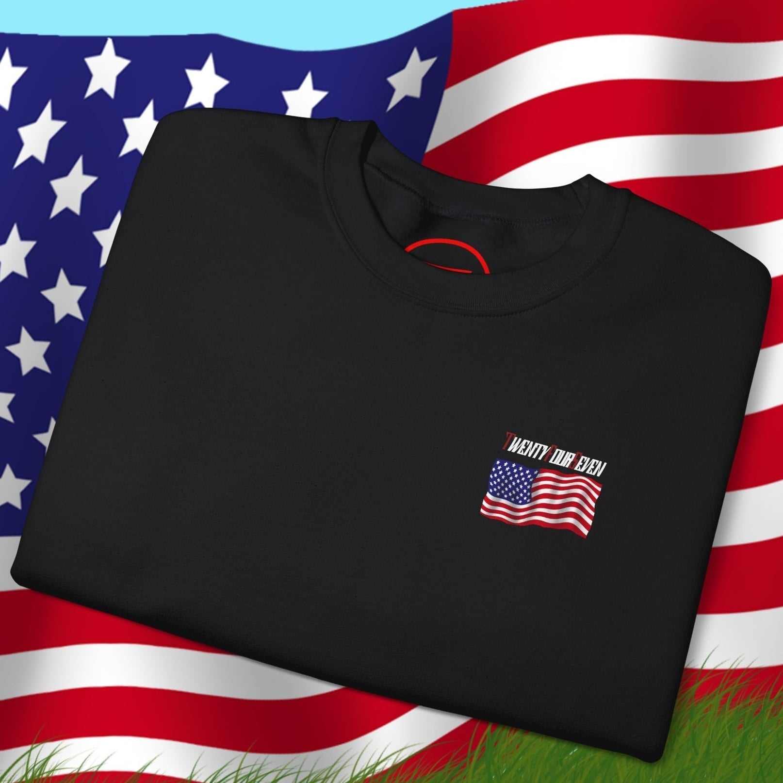 Black US Flag Sweatshirt with small patriotic American flag design folded on grass with large US flag background