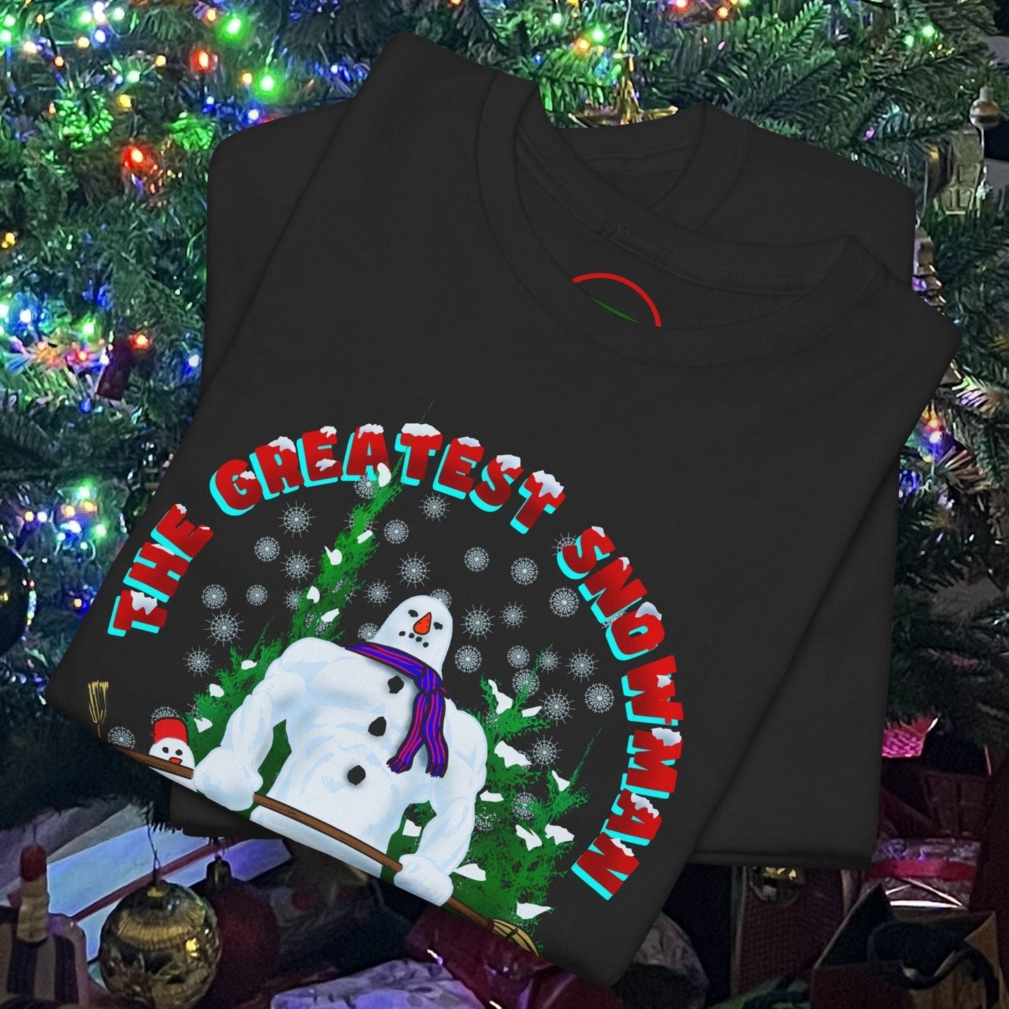 Black snowman gym t-shirt with festive Christmas workout cartoon design and "The Greatest Snowman" text, folded near decorated Christmas tree.