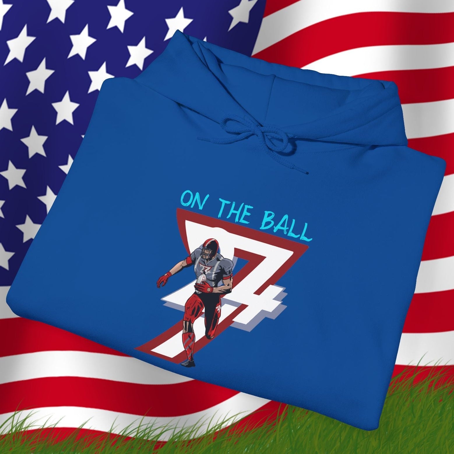 Blue American football hoodie with hand-drawn player design and "On The Ball" text, laid on grass with US flag background