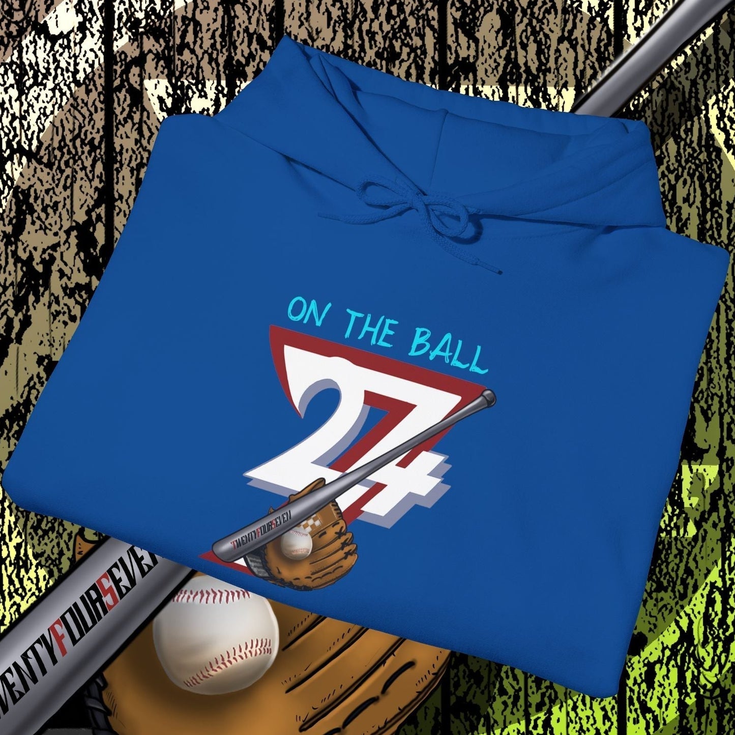 Blue baseball hoodie with "On The Ball 24/7" graphic, baseball bat, glove, and ball design on wooden background