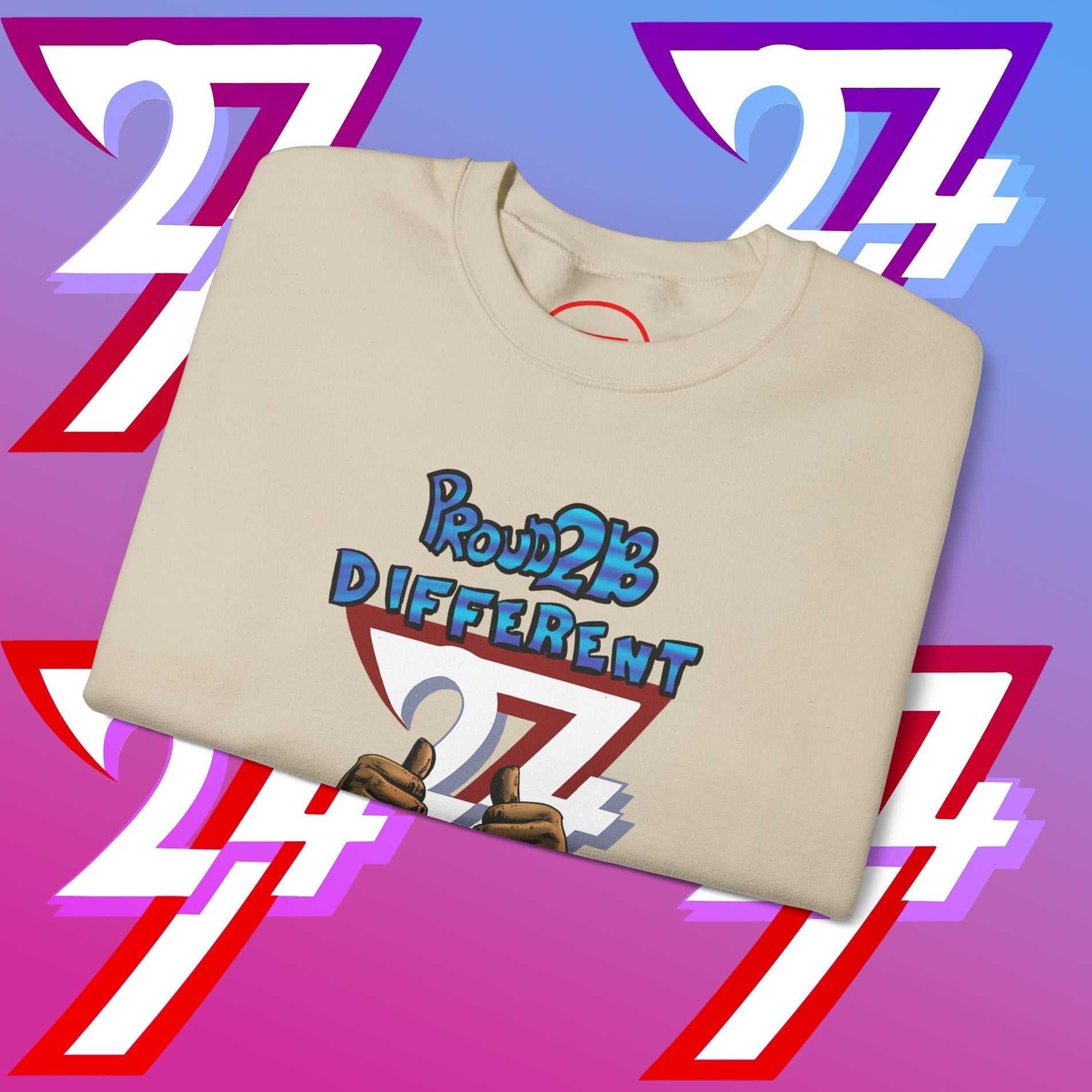 Folded beige artistic sweatshirt with "Proud 2 B Different" slogan and hand-drawn graphic on front against colorful background