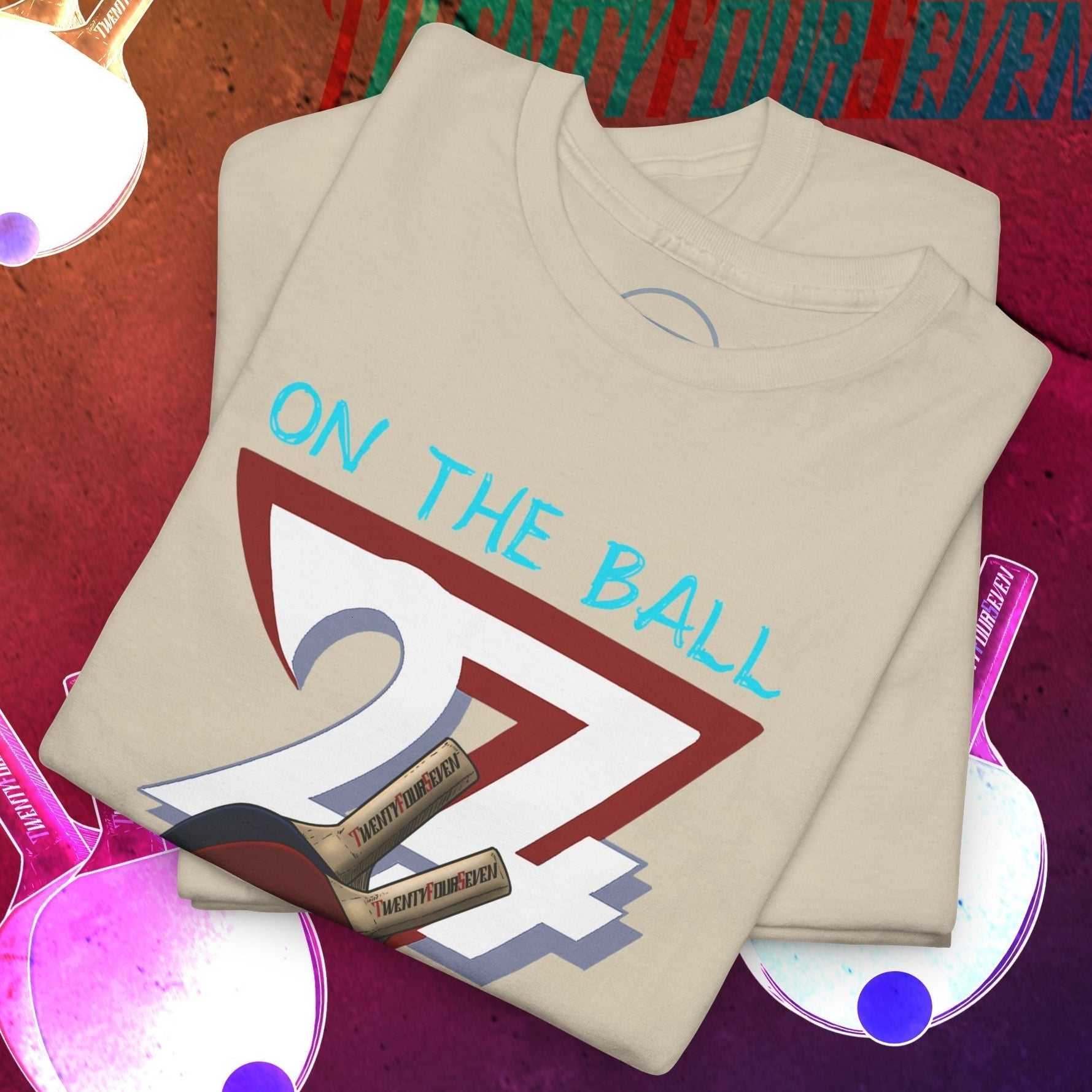 Folded beige ping-pong t-shirt with hand-drawn "On The Ball" sports illustration on a table tennis themed background