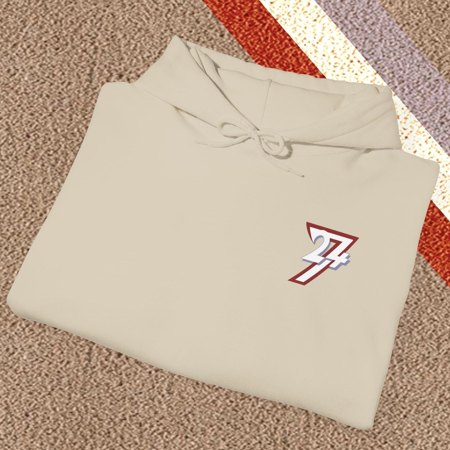 Folded beige stylish hoodie with twentyfourseven logo on textured carpet background