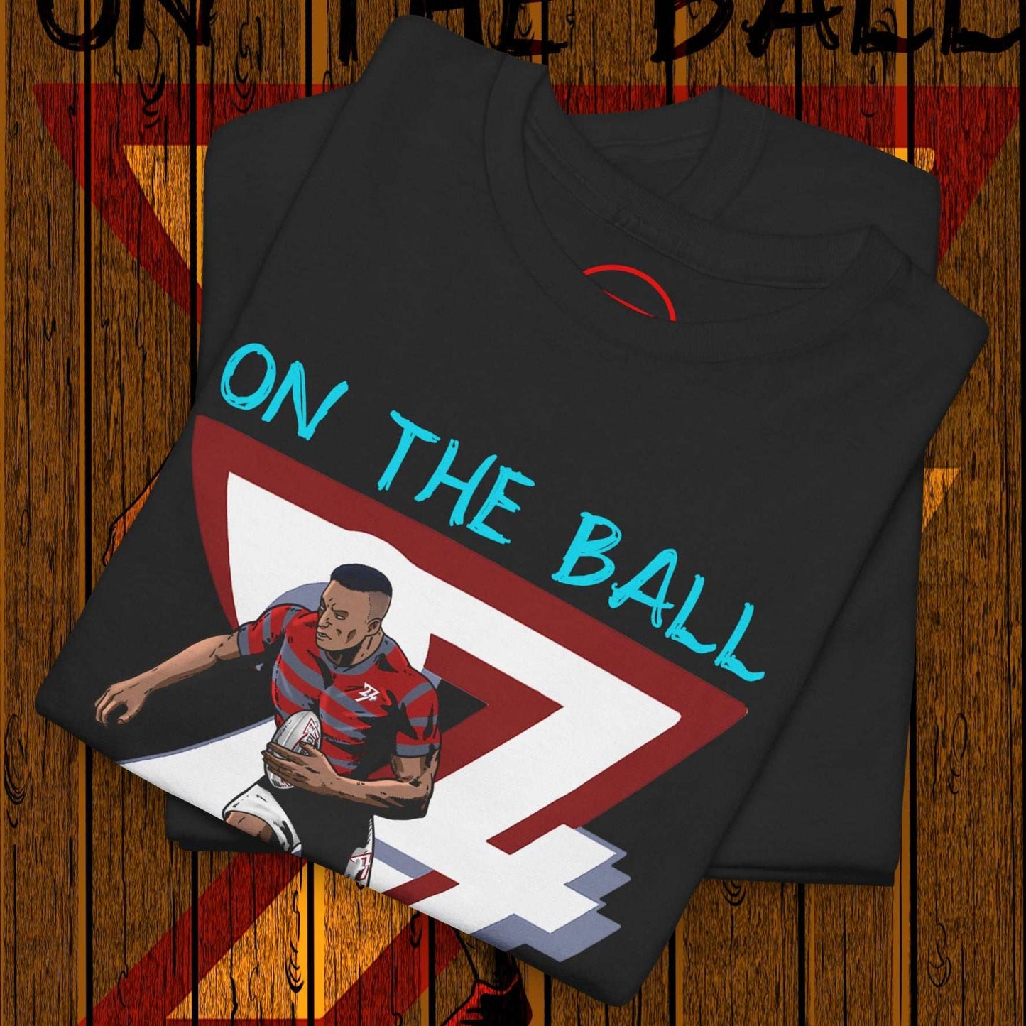 Folded black comic-style rugby player t-shirt with "ON THE BALL" text and dynamic player illustration on wooden background