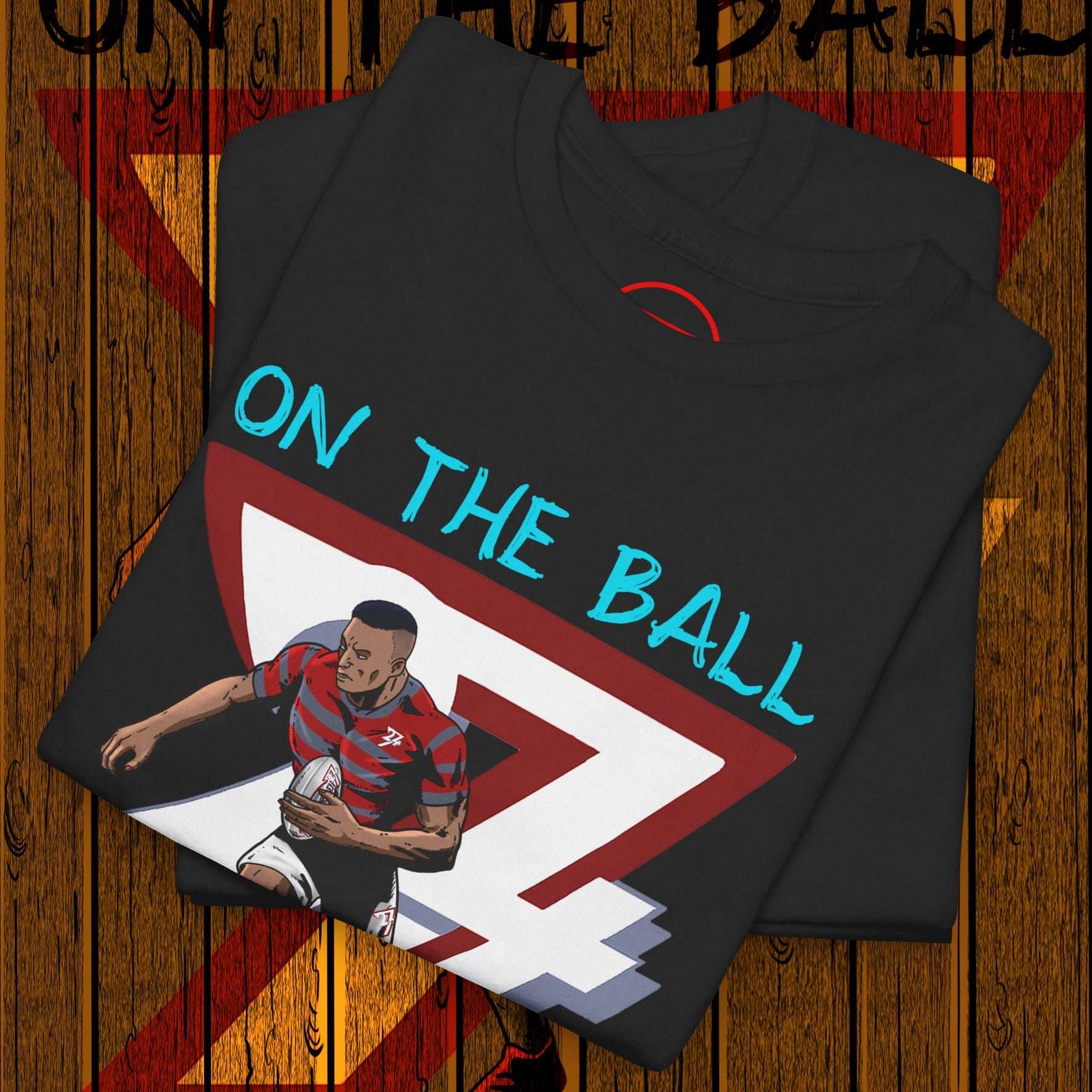 Folded black comic-style rugby player t-shirt with "ON THE BALL" text and dynamic player illustration on wooden background