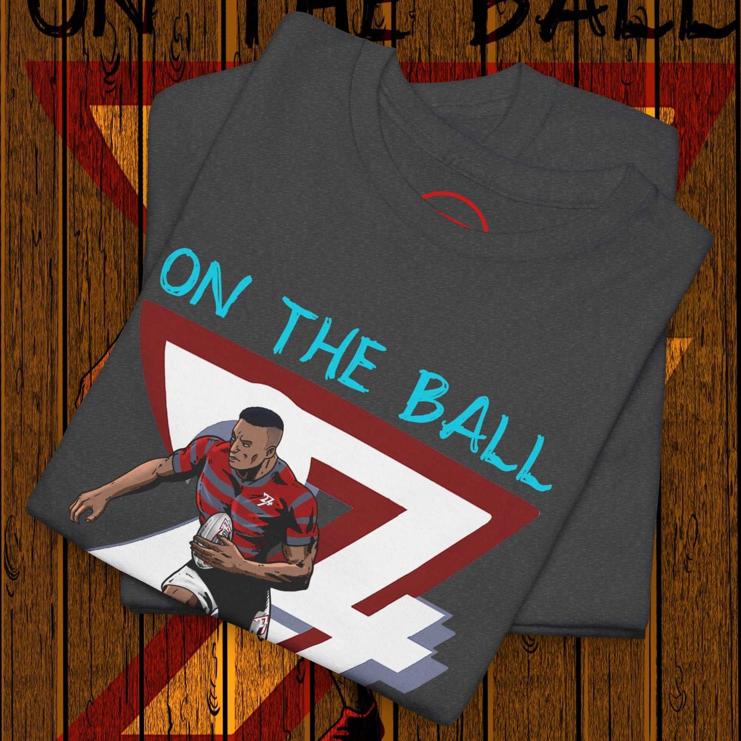 Folded charcoal grey comic-style rugby player t-shirt with "ON THE BALL" text and graphic of player holding rugby ball.