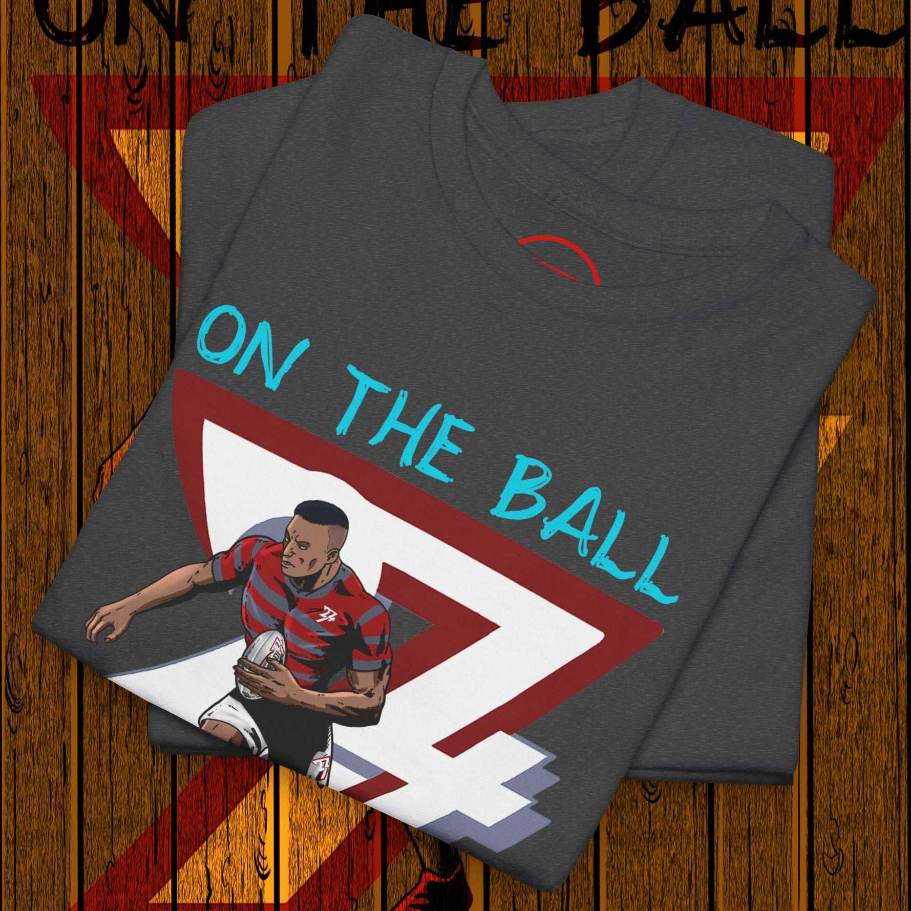 Folded charcoal grey comic-style rugby player t-shirt with "ON THE BALL" text and graphic of player holding rugby ball.