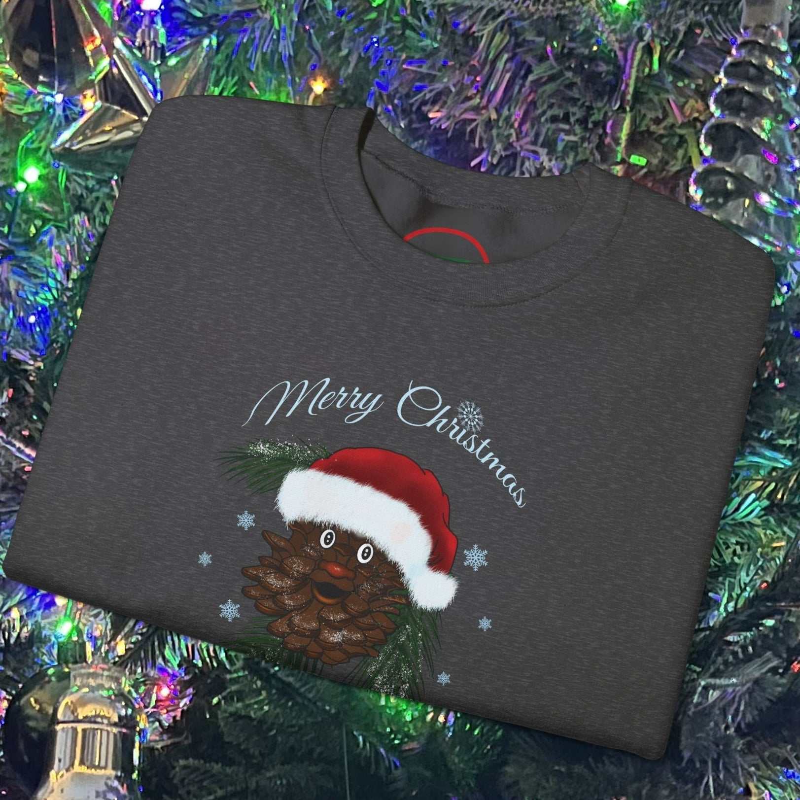 Folded dark gray Santa Pinecone Christmas Sweatshirt with hand-drawn pinecone wearing Santa hat and "Merry Christmas" text on a decorated Christmas tree background