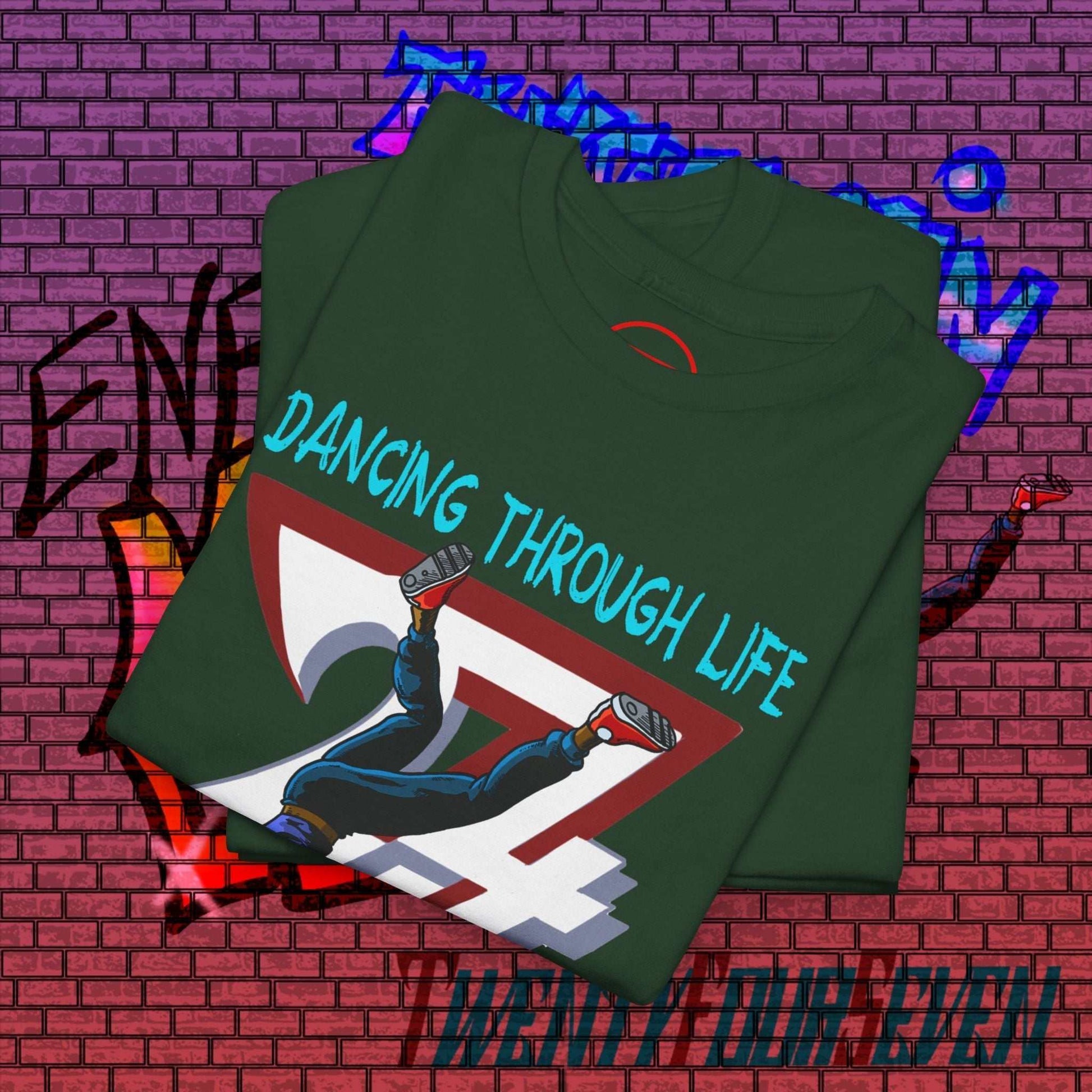 Folded dark green dance graphic t-shirt with hand-drawn street dance illustration and "Dancing Through Life" text on urban brick wall background