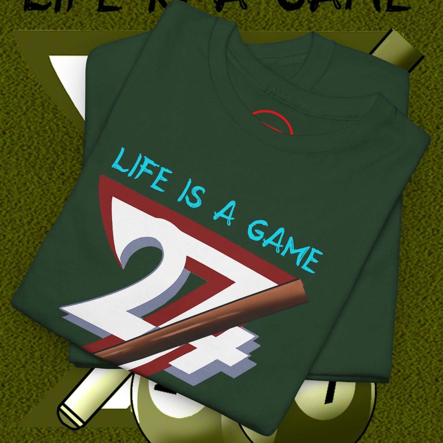 Folded green billiards tee with "Life is a Game" and pool cue graphic on front, laid over billiard balls and cues background
