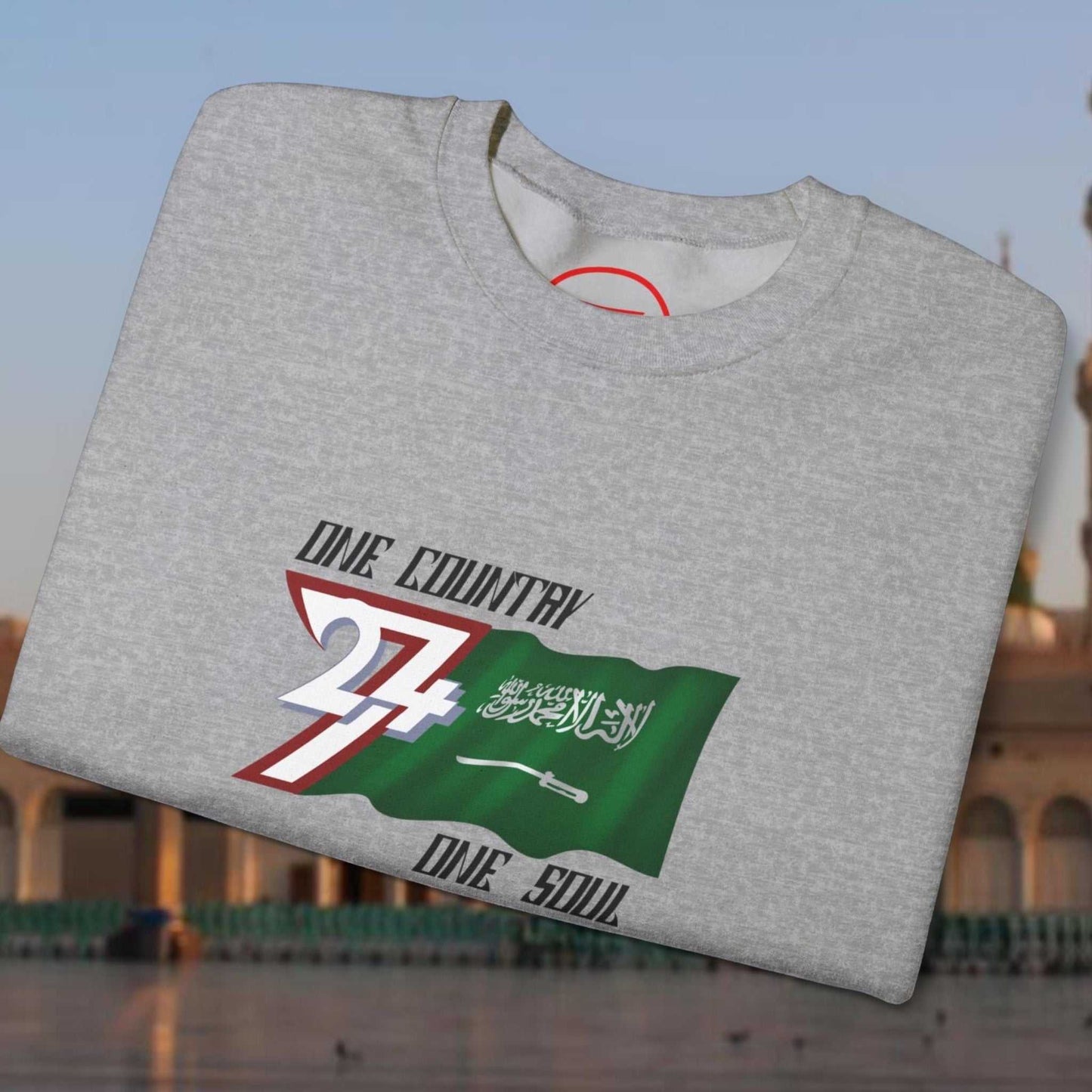 Folded grey crewneck sweatshirt with vibrant hand-drawn Saudi Arabia flag and "One Country One Soul" text design
