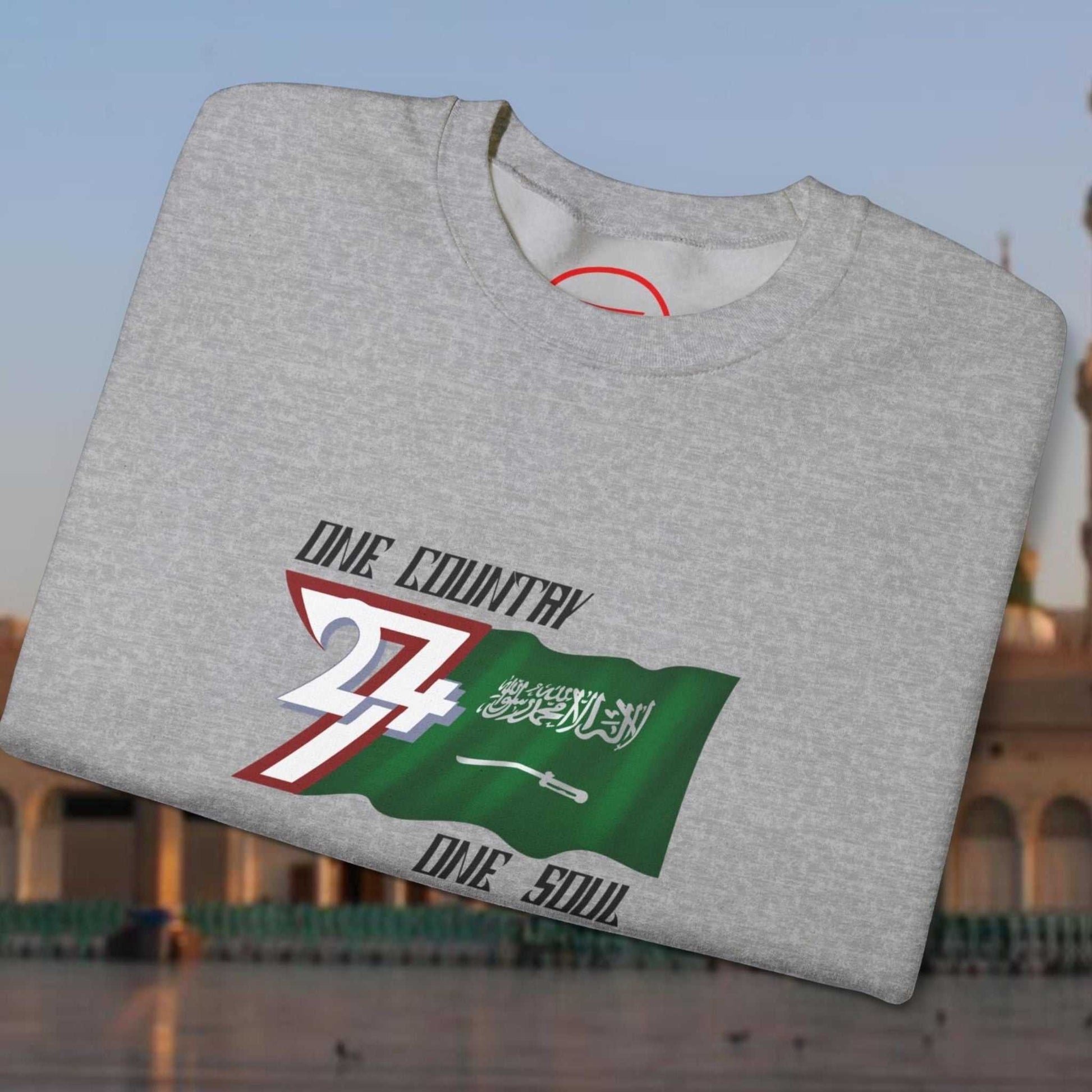 Folded grey crewneck sweatshirt with vibrant hand-drawn Saudi Arabia flag and "One Country One Soul" text design