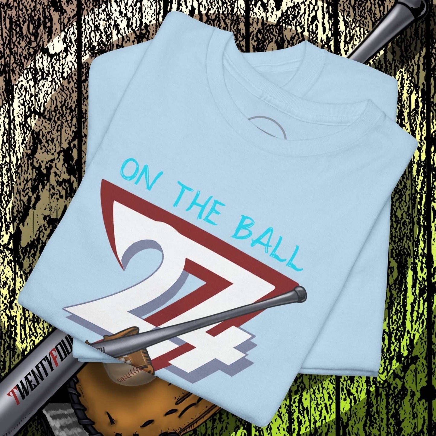 Folded light blue baseball illustrated tee with "On The Ball 24/7" graphic, baseball bat and glove background, casual sportswear design.