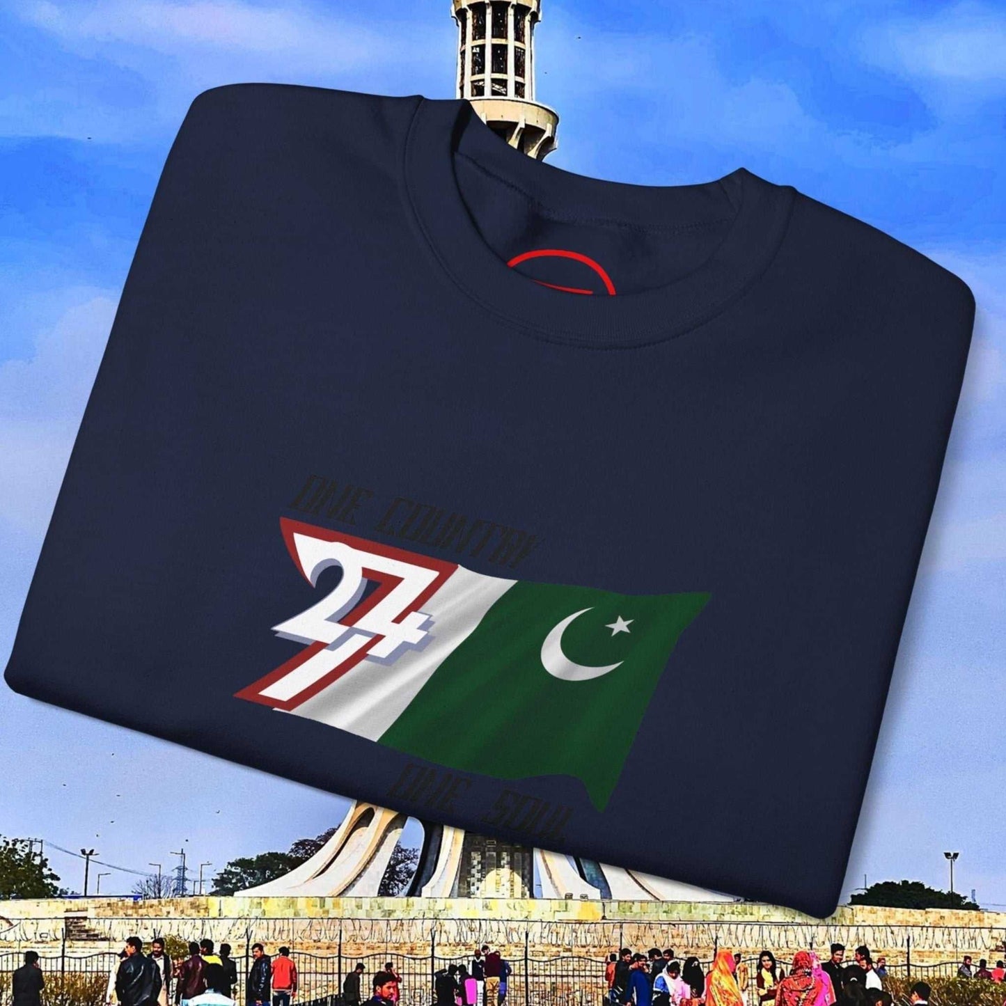 Folded navy Pakistan Flag Sweatshirt with hand-drawn flag graphic and slogan displayed outdoors near Minar-e-Pakistan monument