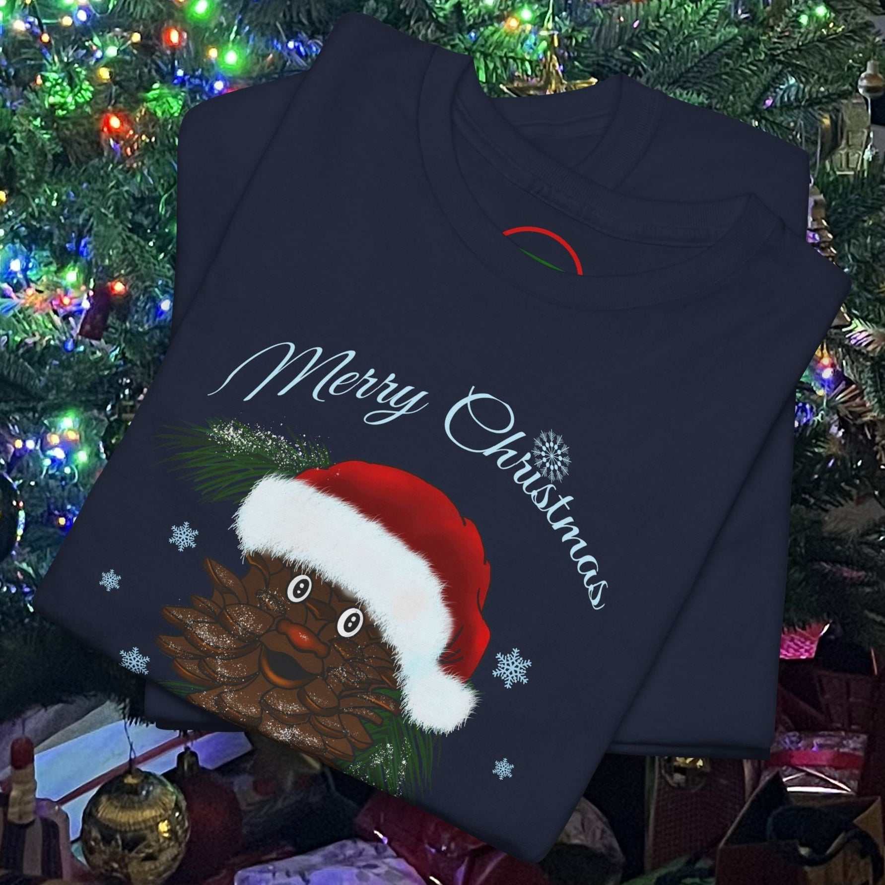 Folded navy Santa Pinecone Tee with cartoon pinecone wearing Santa hat and "Merry Christmas" text by Christmas tree lights