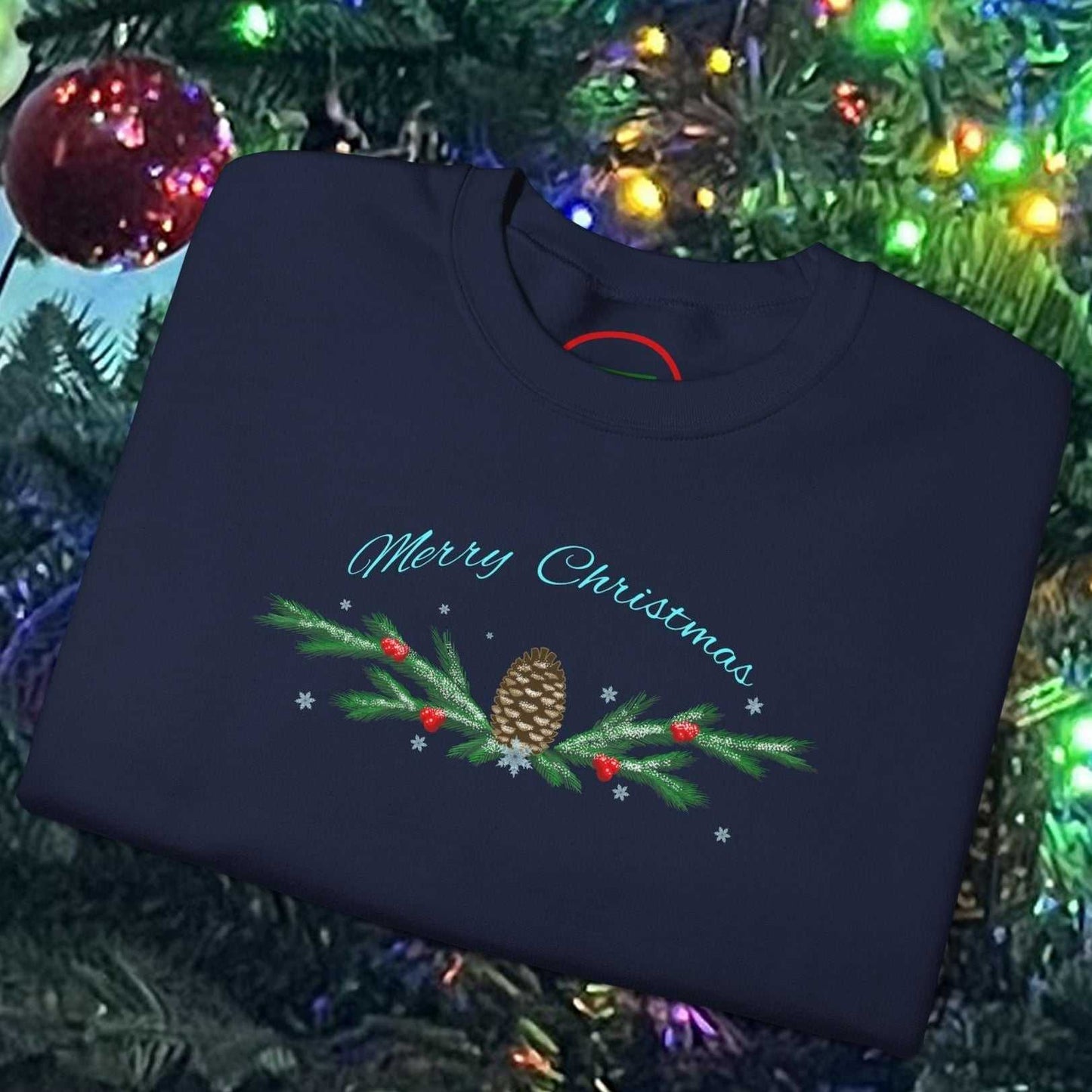 Folded navy blue Pinecone Christmas Sweatshirt with festive pinecone and greenery design, placed on decorated Christmas tree background.