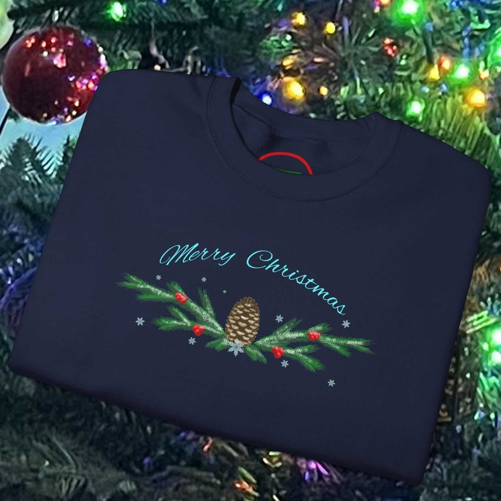 Folded navy blue Pinecone Christmas Sweatshirt with festive pinecone and greenery design, placed on decorated Christmas tree background.