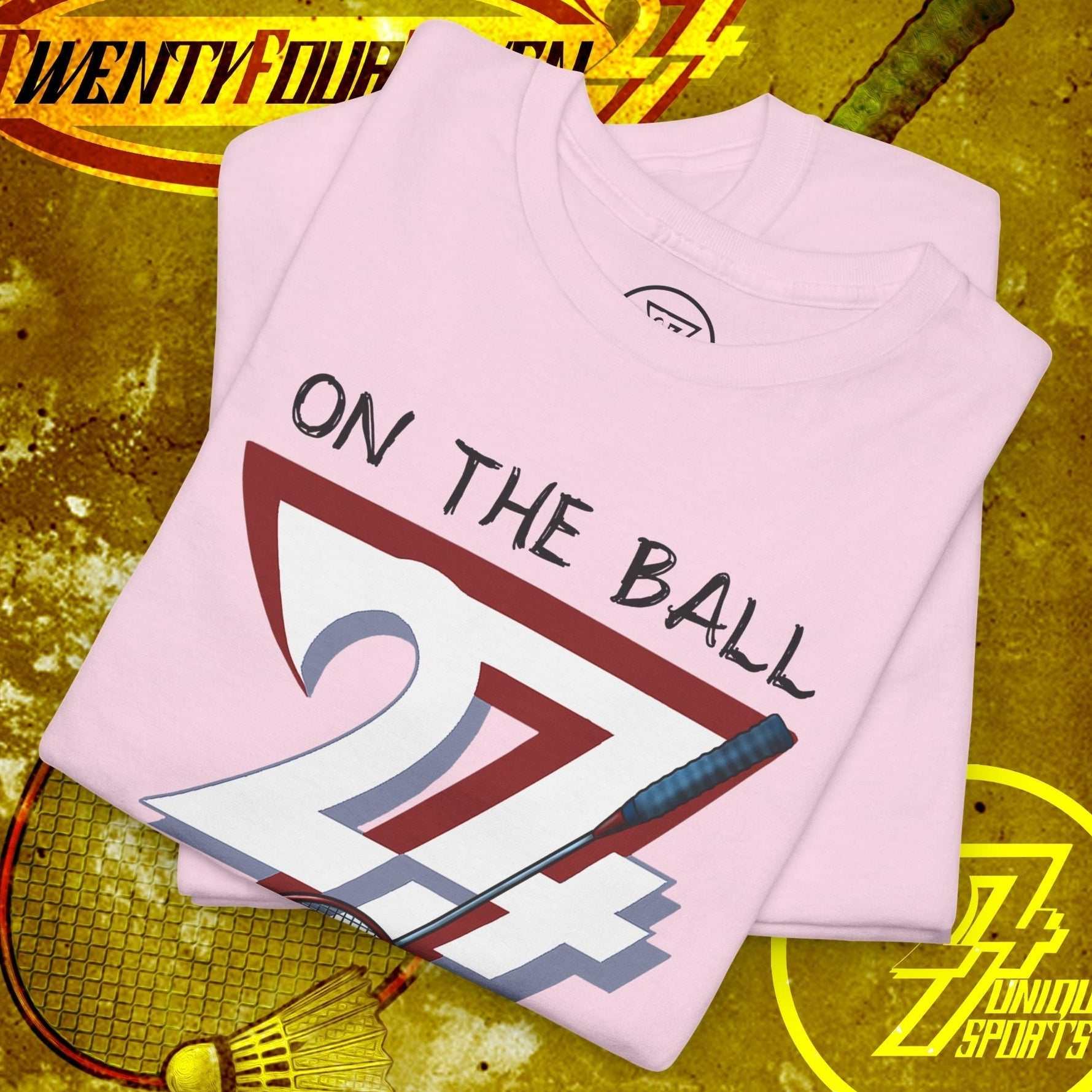 Folded pink badminton tee with hand-drawn "On The Ball 24/7" design and shuttlecock illustration
