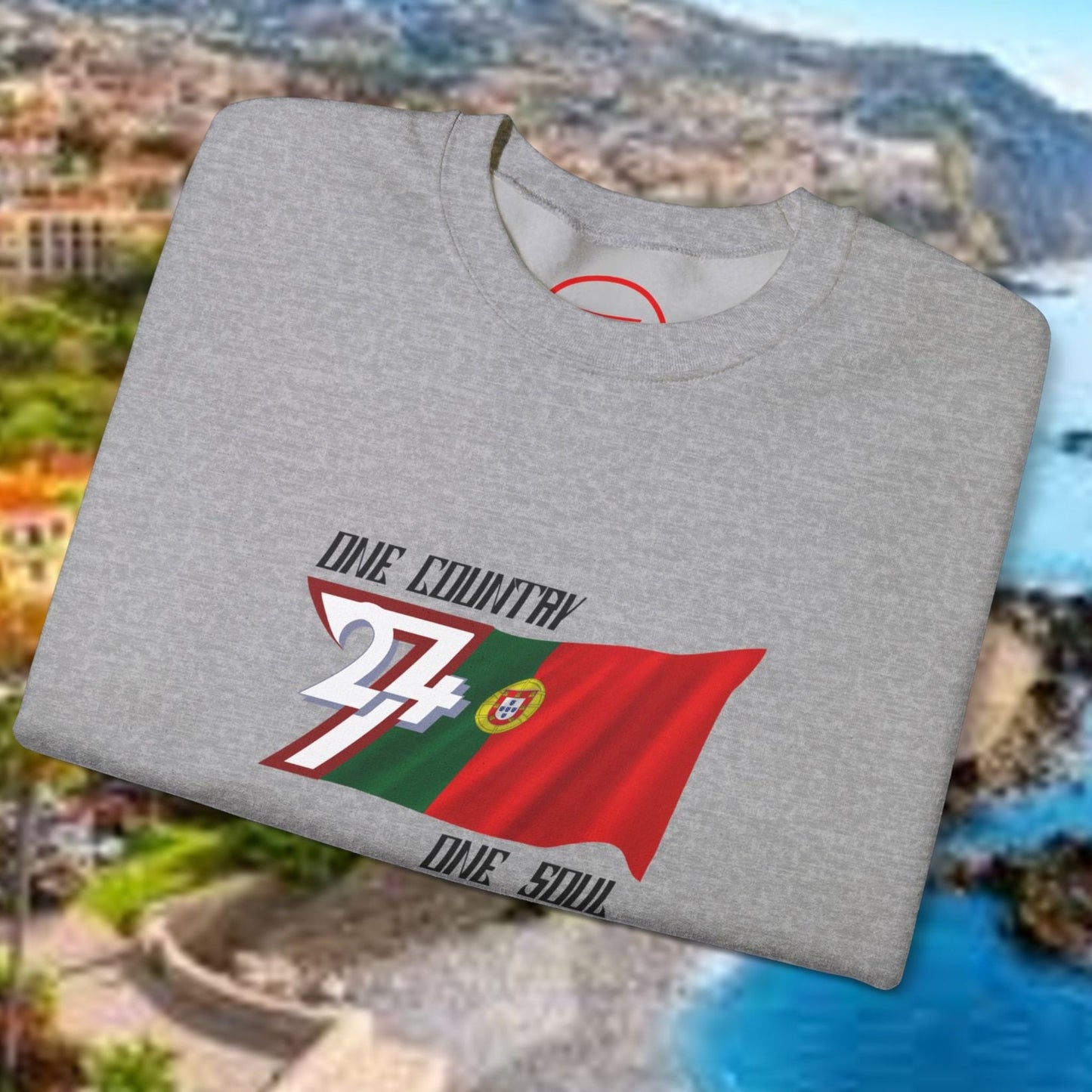 Gray Portugal flag sweatshirt with vibrant hand-drawn football World Cup design folded on scenic coastal background