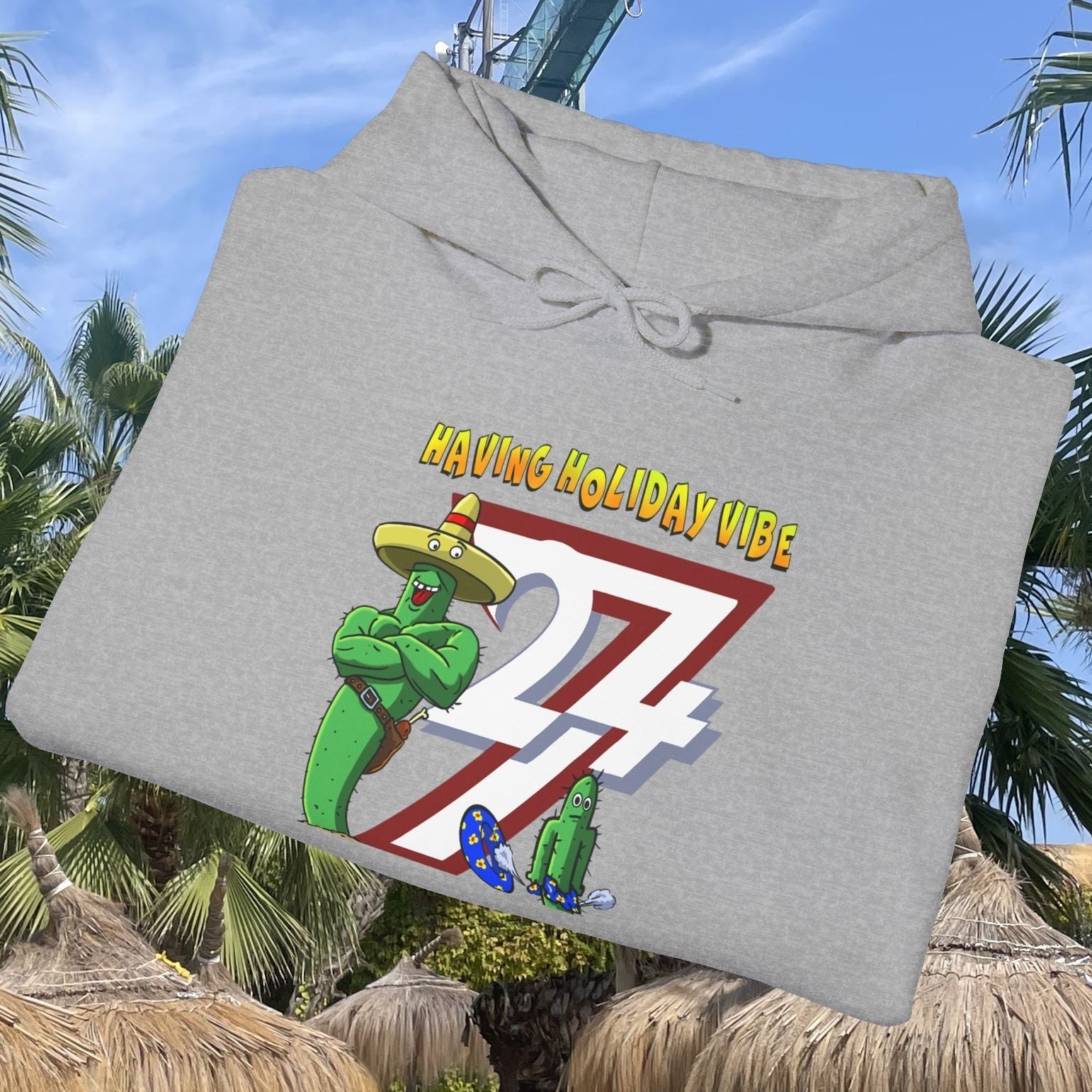 Gray cactus hoodie with cartoon design and "Having Holiday Vibe" text, folded outdoors