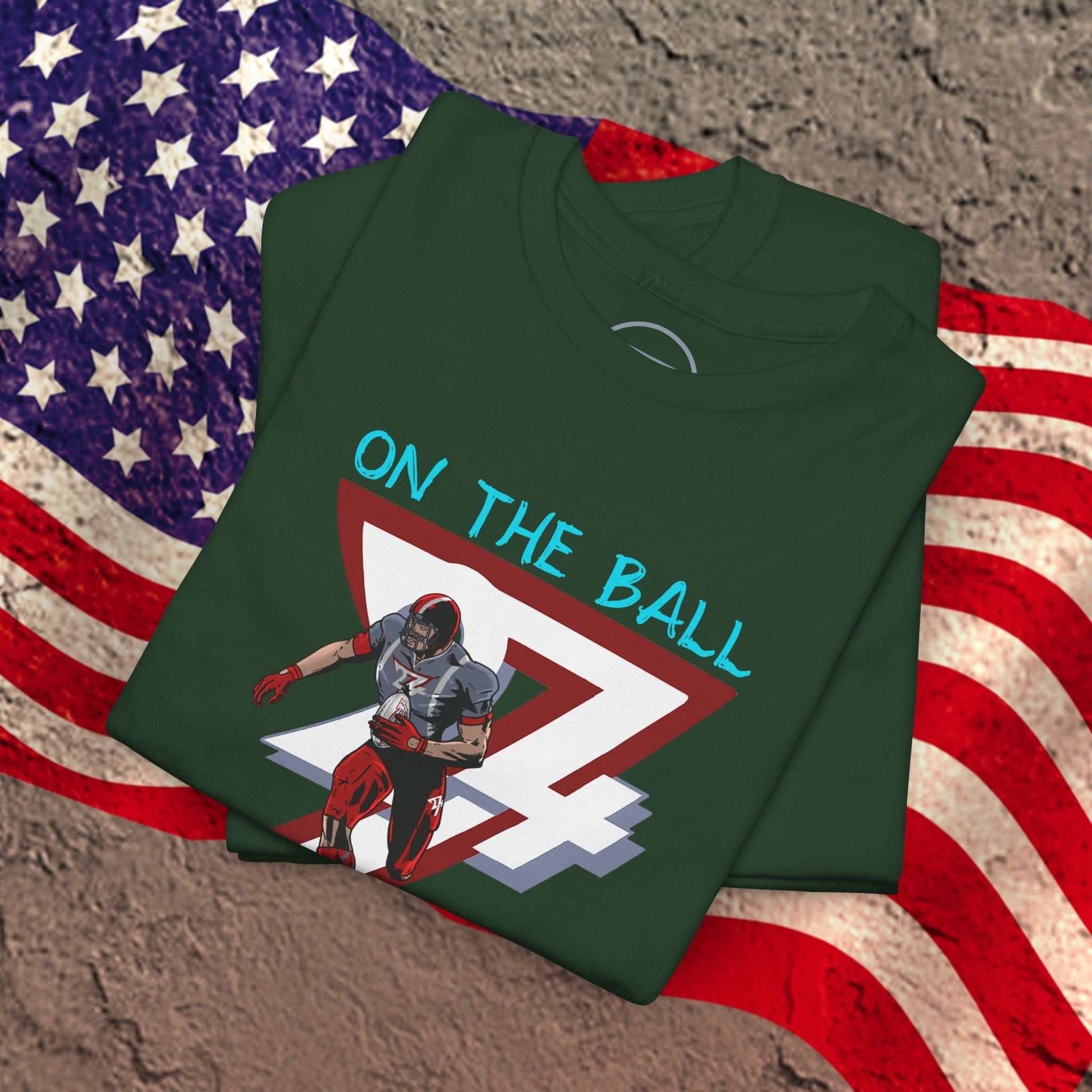 Green American football tee with hand-drawn comic-style player graphic and "ON THE BALL" text, folded on US flag background