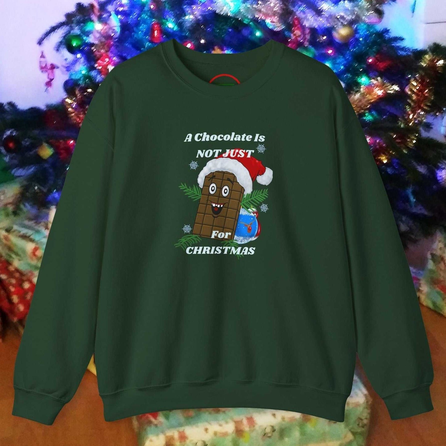 Green Christmas chocolate sweatshirt with funny cartoon character wearing Santa hat and festive text design in front of decorated Christmas tree and presents