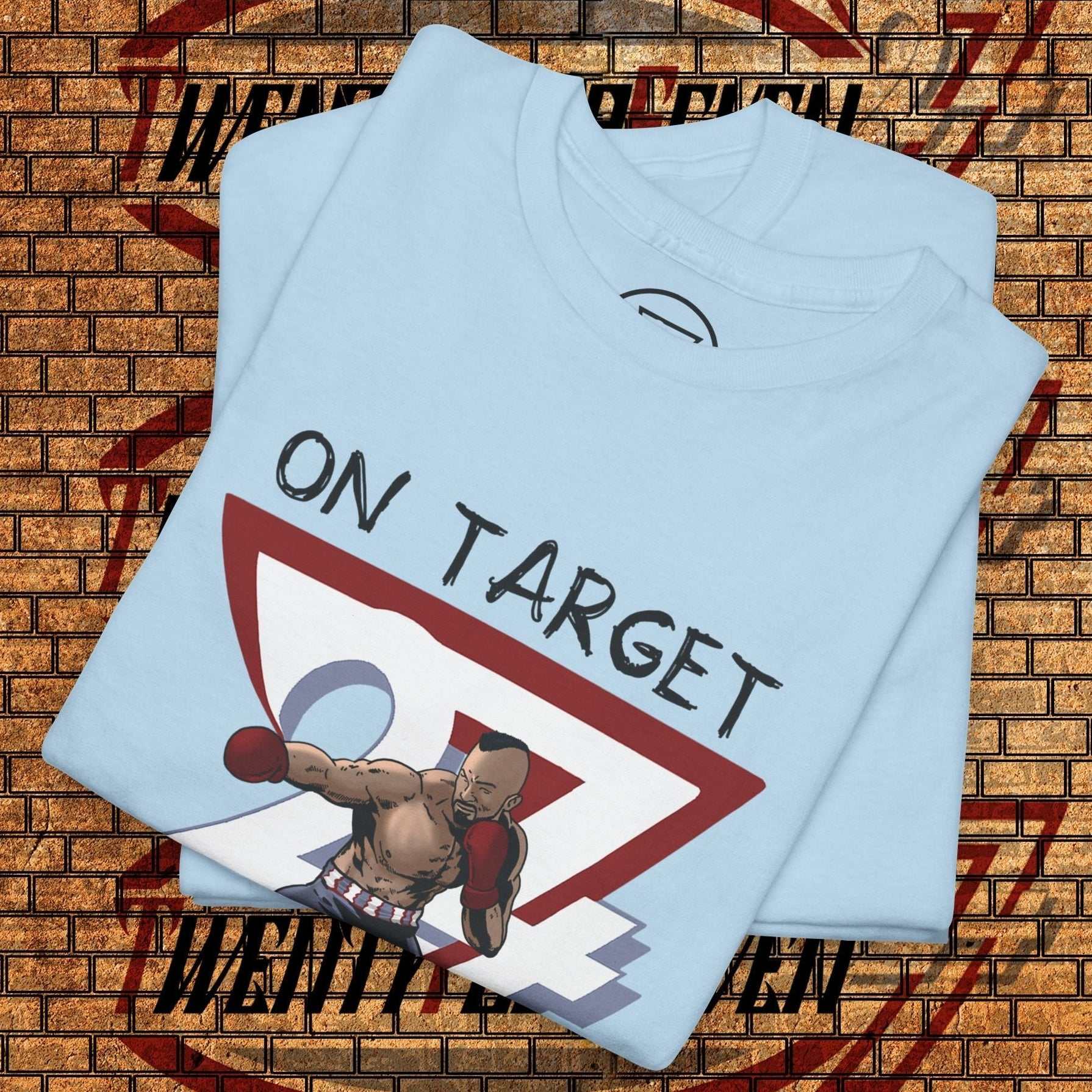 Light blue boxing graphic shirt with hand-drawn boxer illustration and "ON TARGET" text, folded on brick wall background