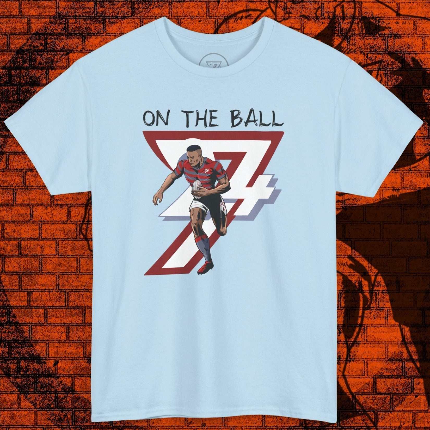 Light blue rugby sports tee with hand-drawn rugby player illustration and "On The Ball" text.