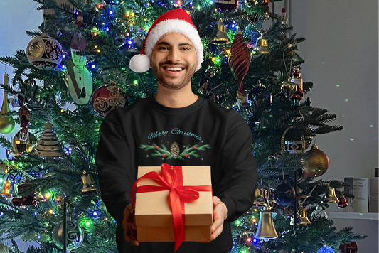 Man wearing Pinecone Christmas Sweatshirt and Santa hat holding gift box in front of decorated Christmas tree