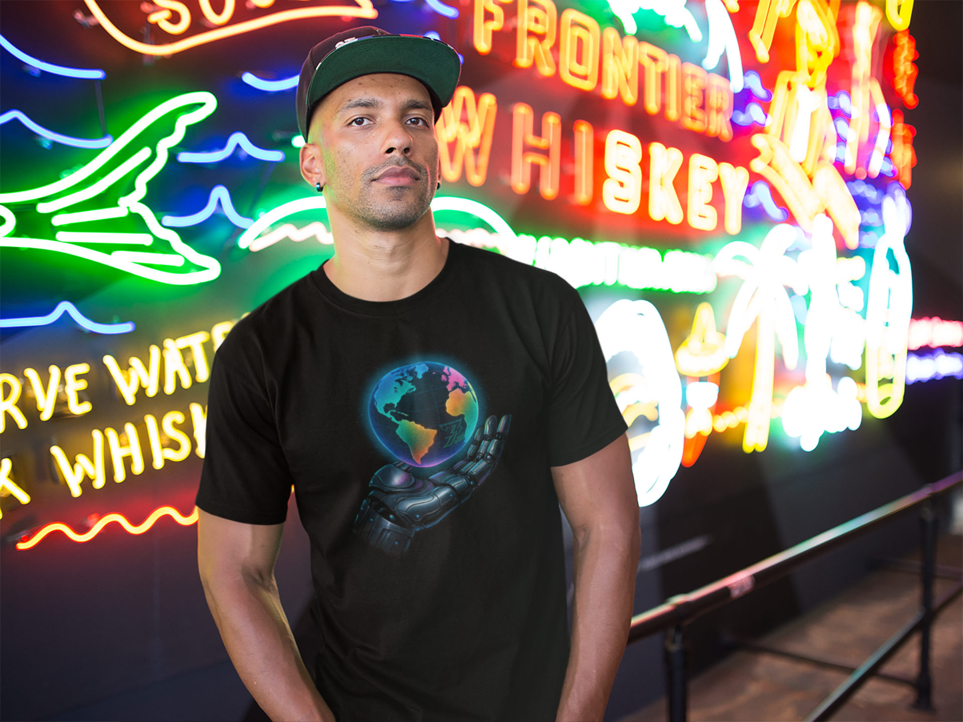 Man wearing a black futuristic tee with vibrant sci-fi robotic hand holding a glowing Earth design in neon-lit setting
